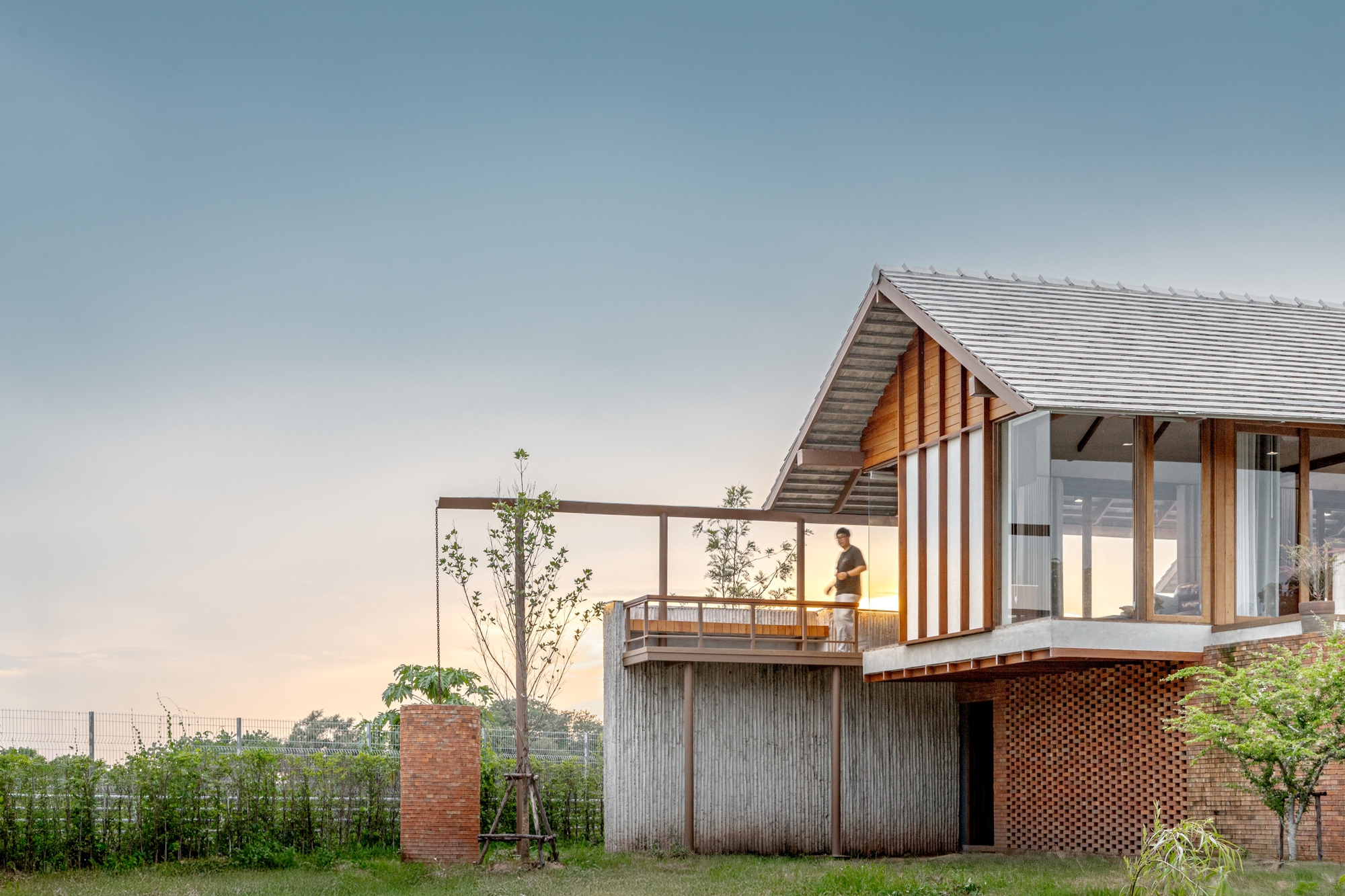 Elevated timber pavilion on perforated brick and concrete base with person on balcony at dusk