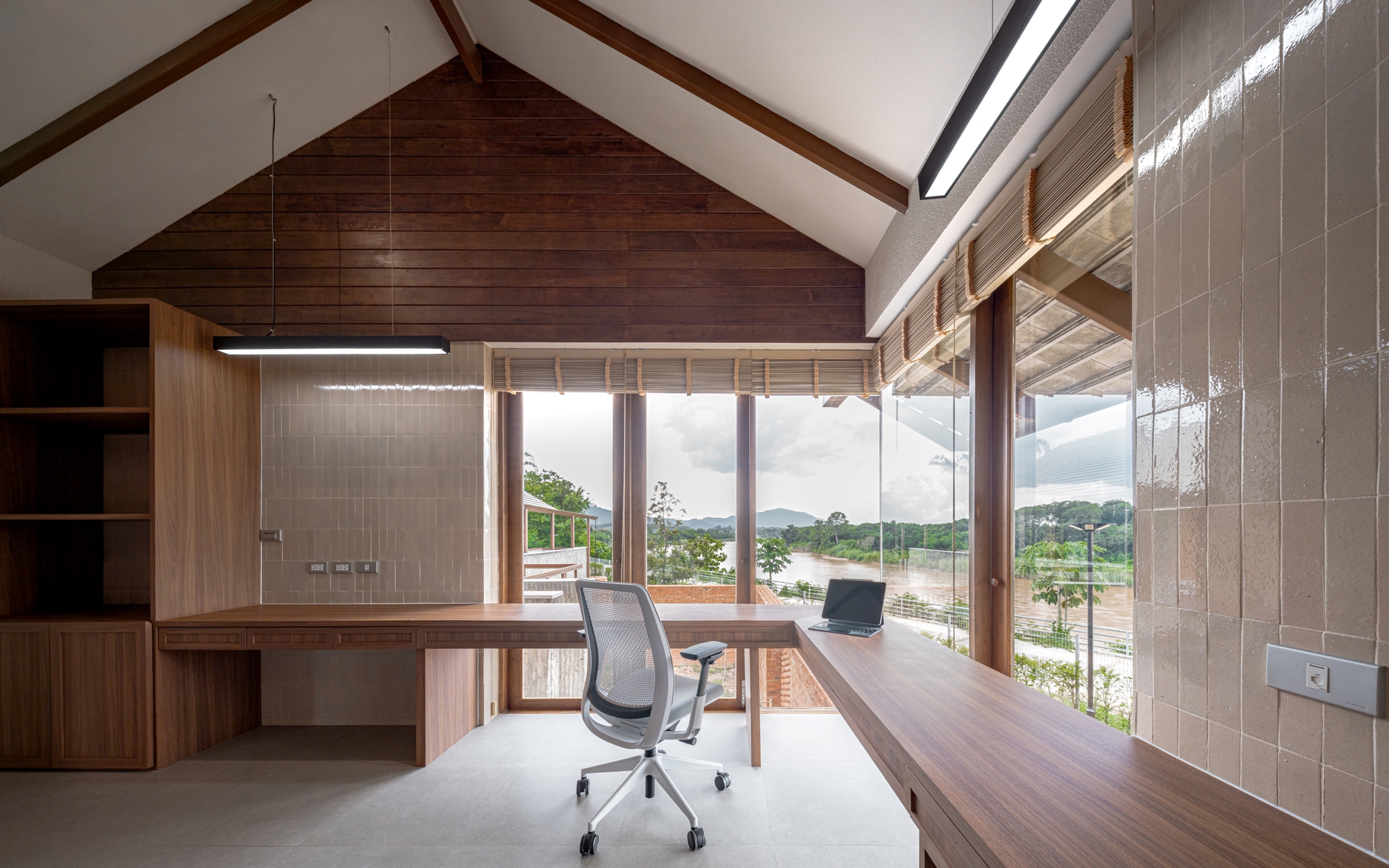 Home office with timber desk and pitched ceiling overlooking the river through floor-to-ceiling windows