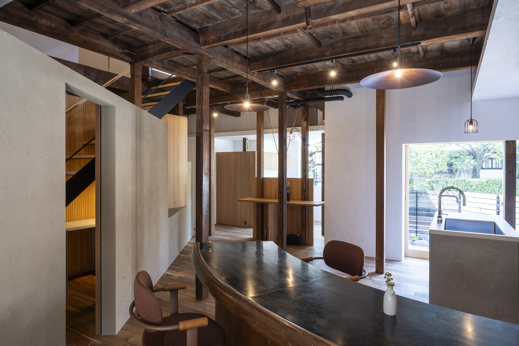 Open kitchen and dining area beneath exposed timber beams with pendant lights and doorway to terrace