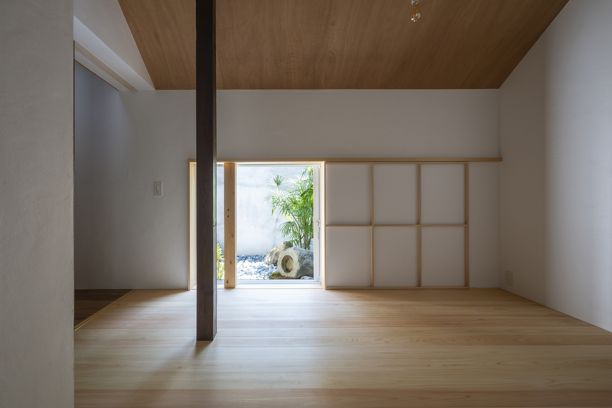 Light-filled room with timber floors, shoji screen and framed opening to a small courtyard garden