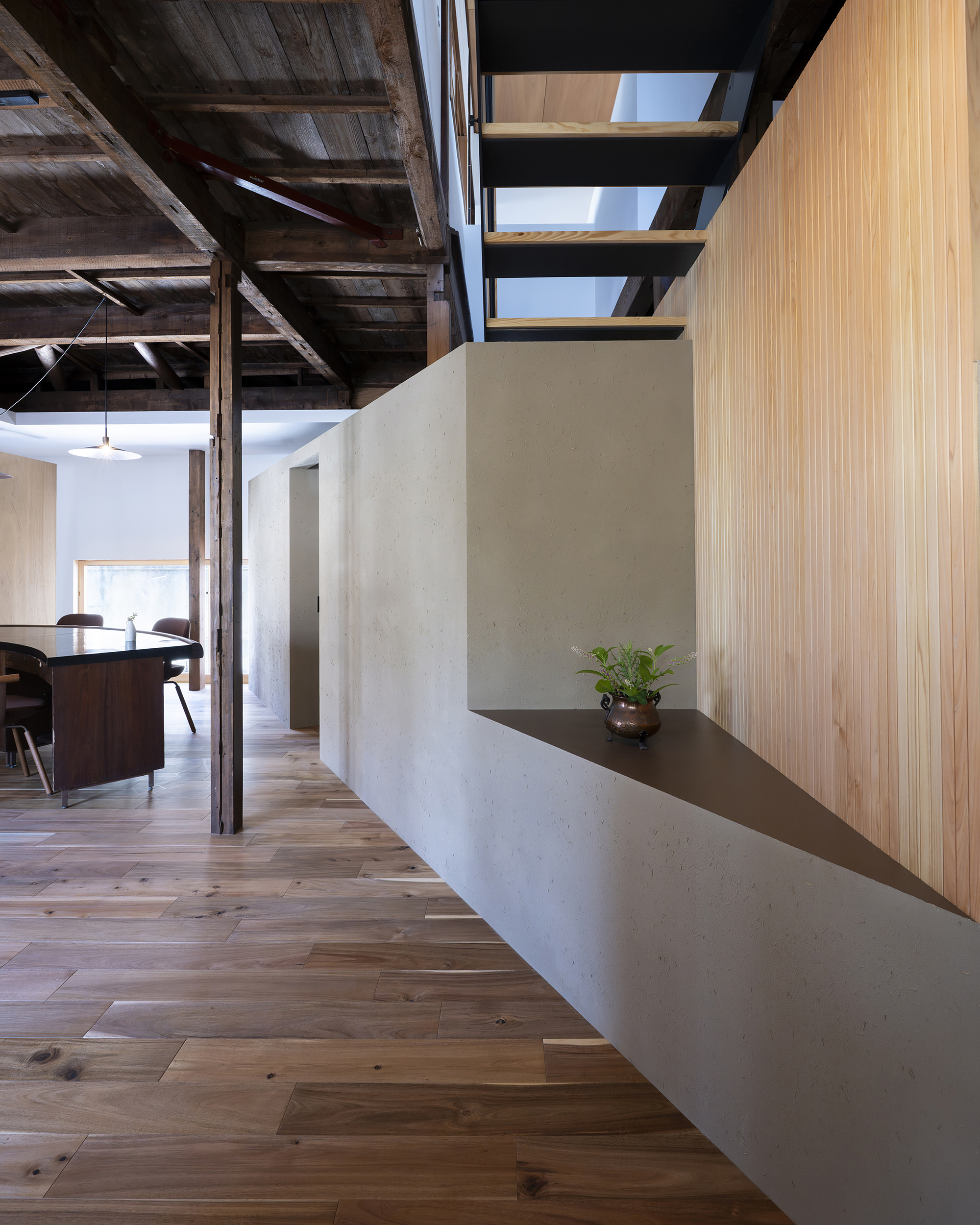 Open-tread steel staircase rising above a white plaster volume with light wood flooring below