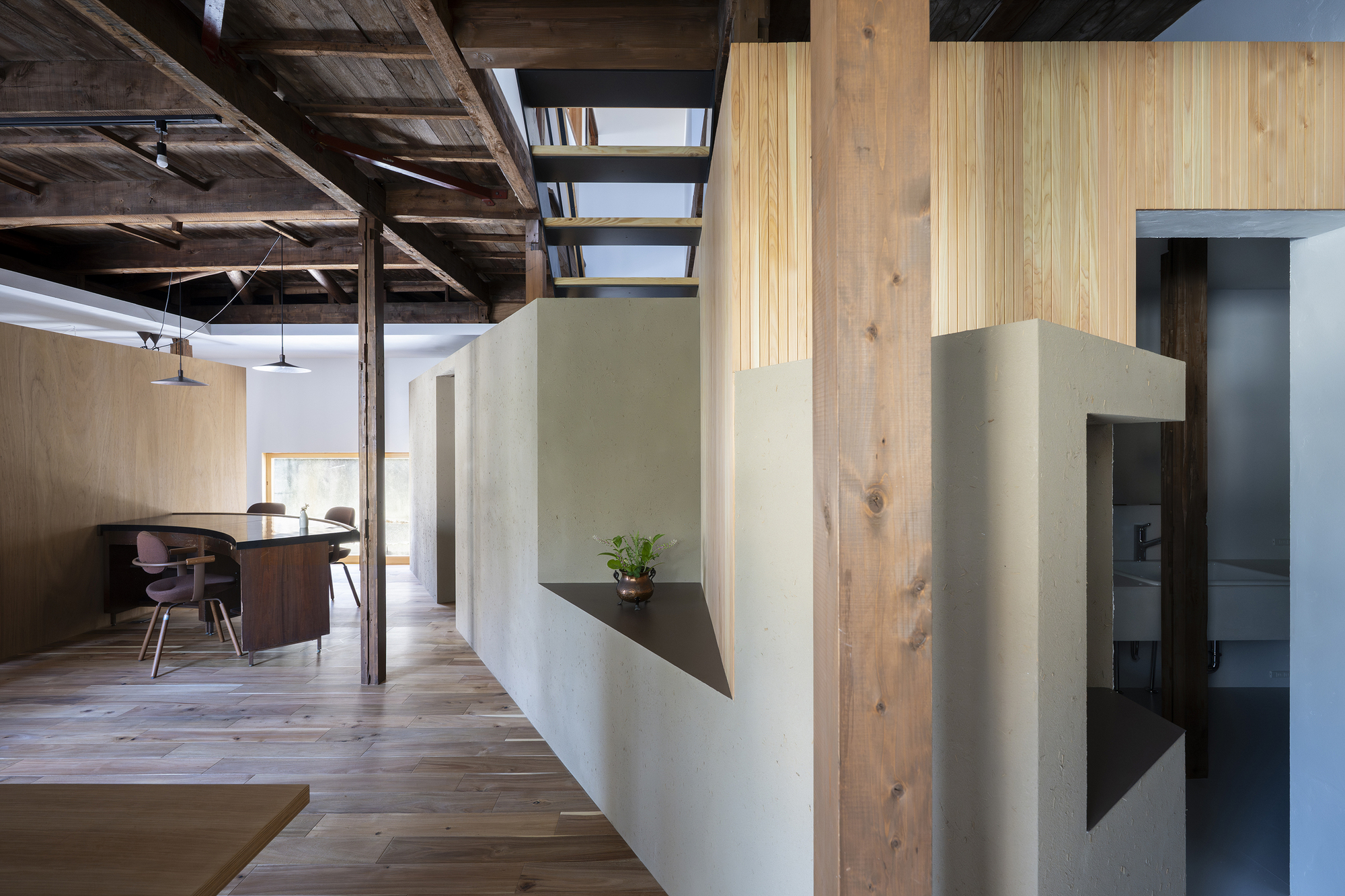 White plaster wall with triangular steel shelf holding a small plant beneath timber beams