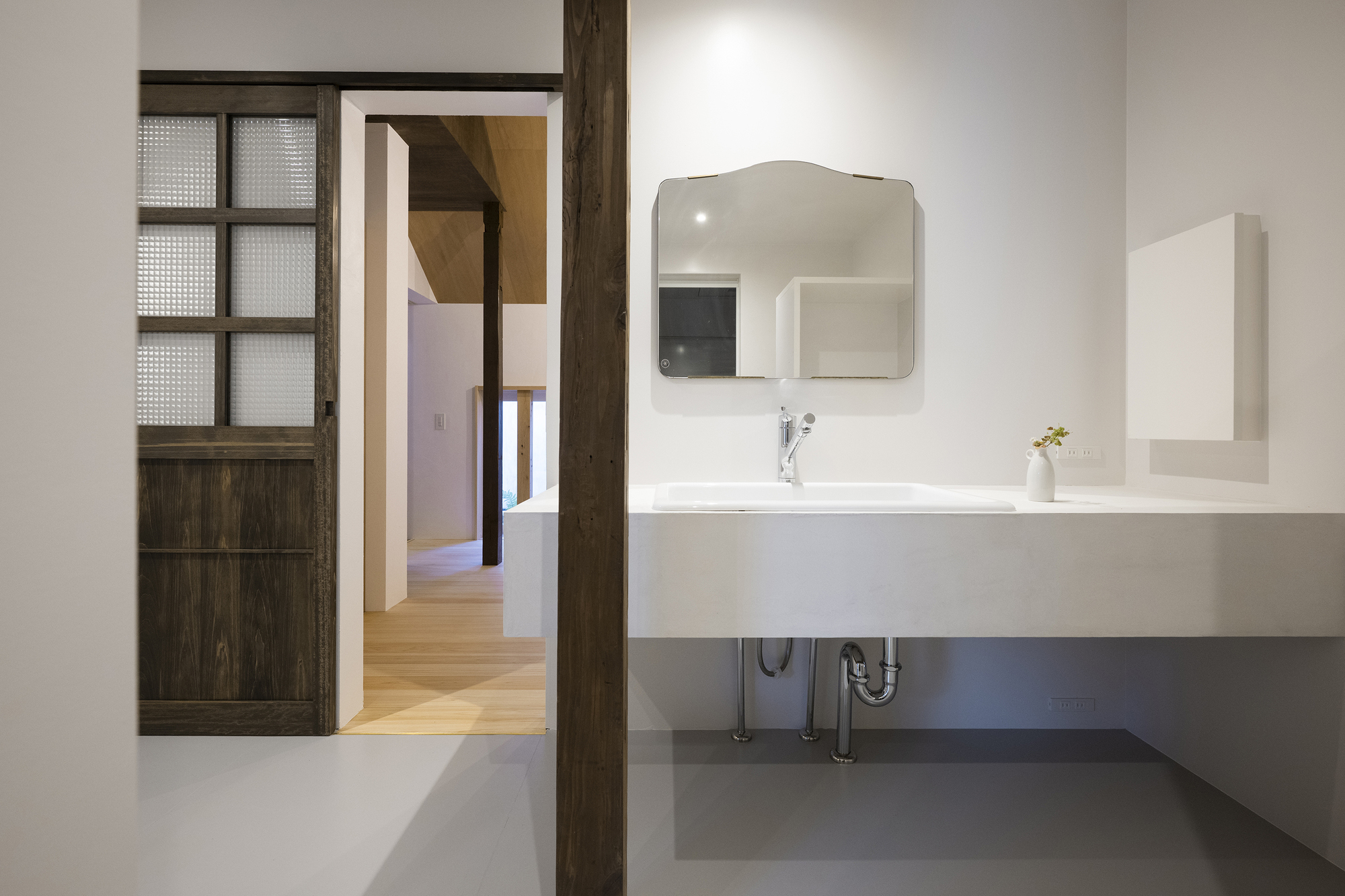 Bathroom vanity with floating white sink and curved mirror beside a sliding timber and glass door