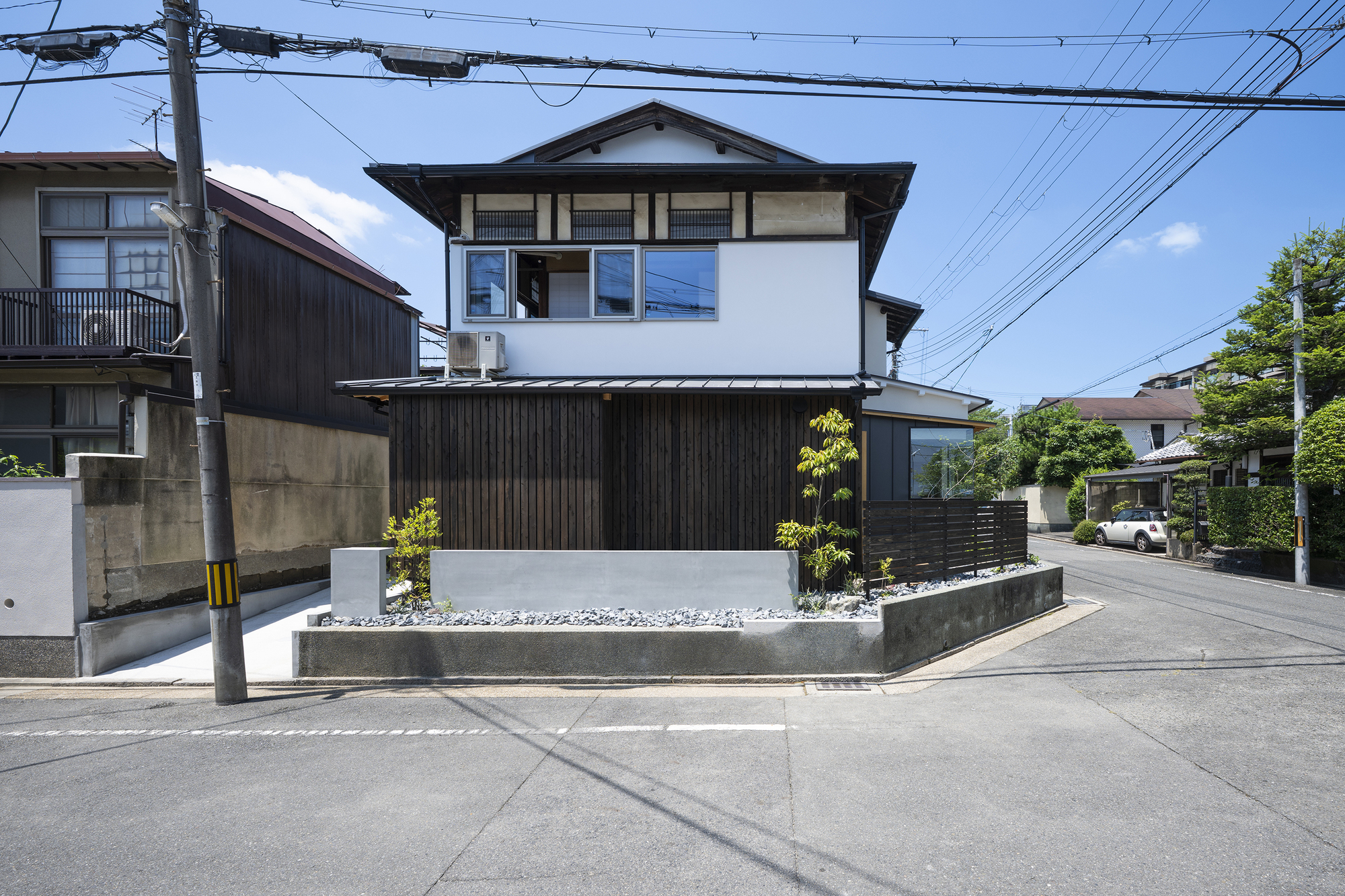 Two-story facade with white upper level and charcoal timber cladding at street level beneath overhead wires