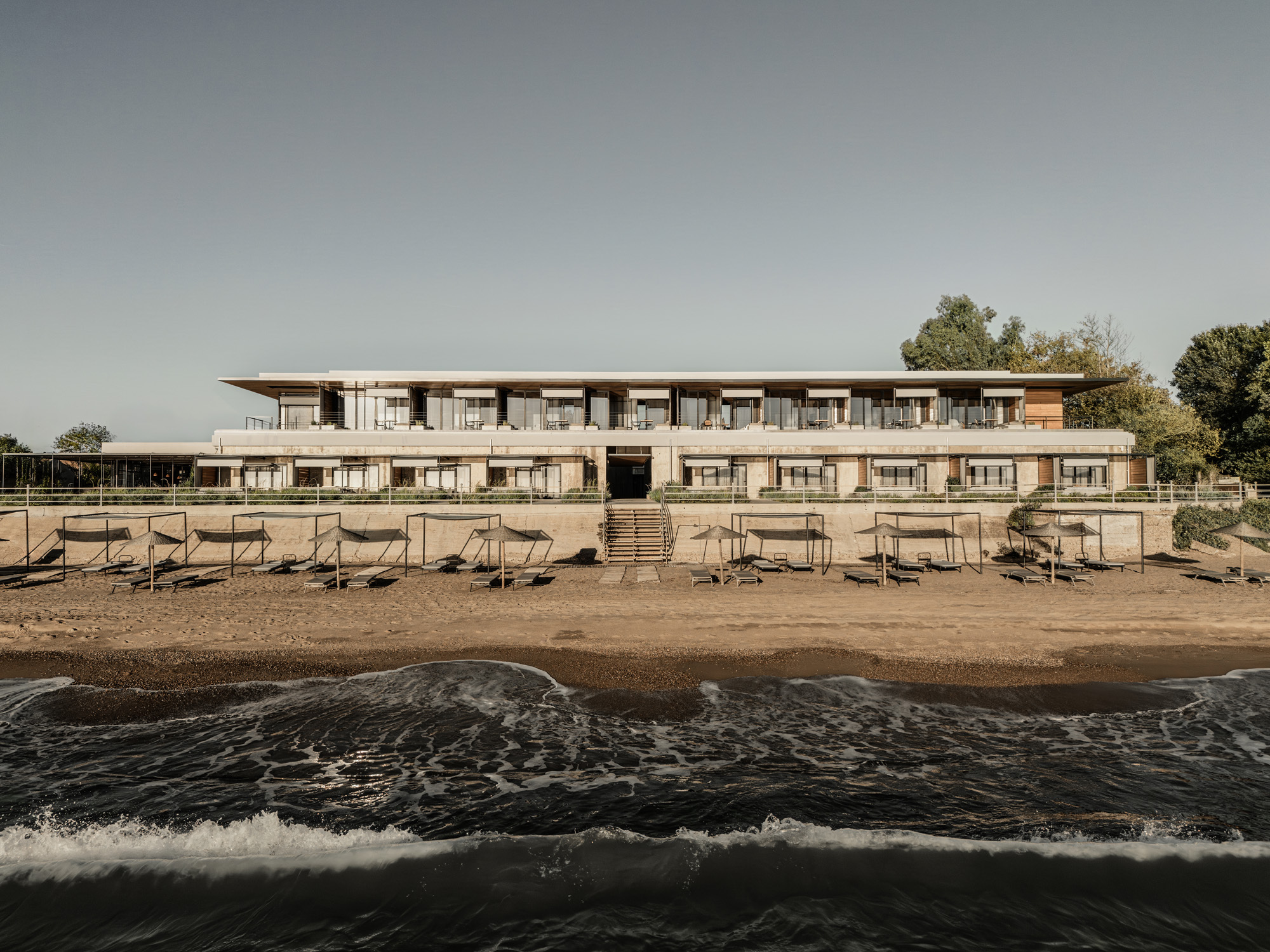 Two-story beachfront facade with horizontal balconies and timber cladding viewed from the water's edge