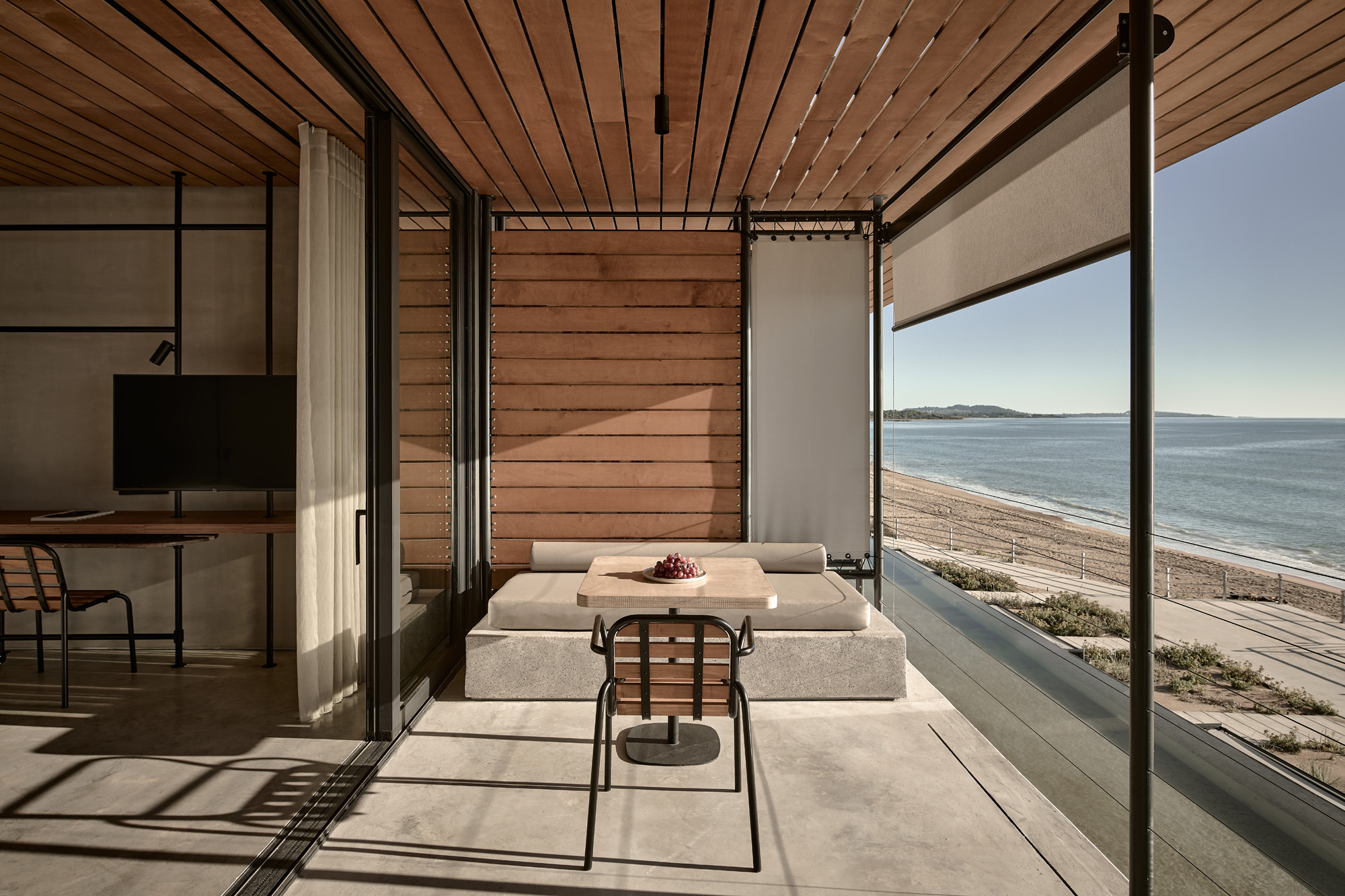 Living area with concrete flooring and full-height glazing framing the beachfront and distant hills
