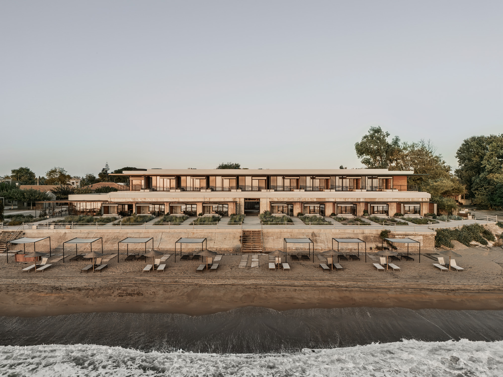 Beachfront facade with rows of lounge chairs on sand and gentle surf at dusk