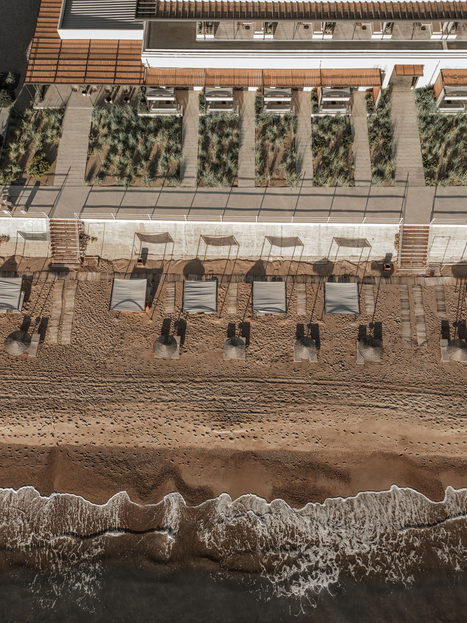 Aerial view of timber cabanas and planted terrace beds between beach and building edge