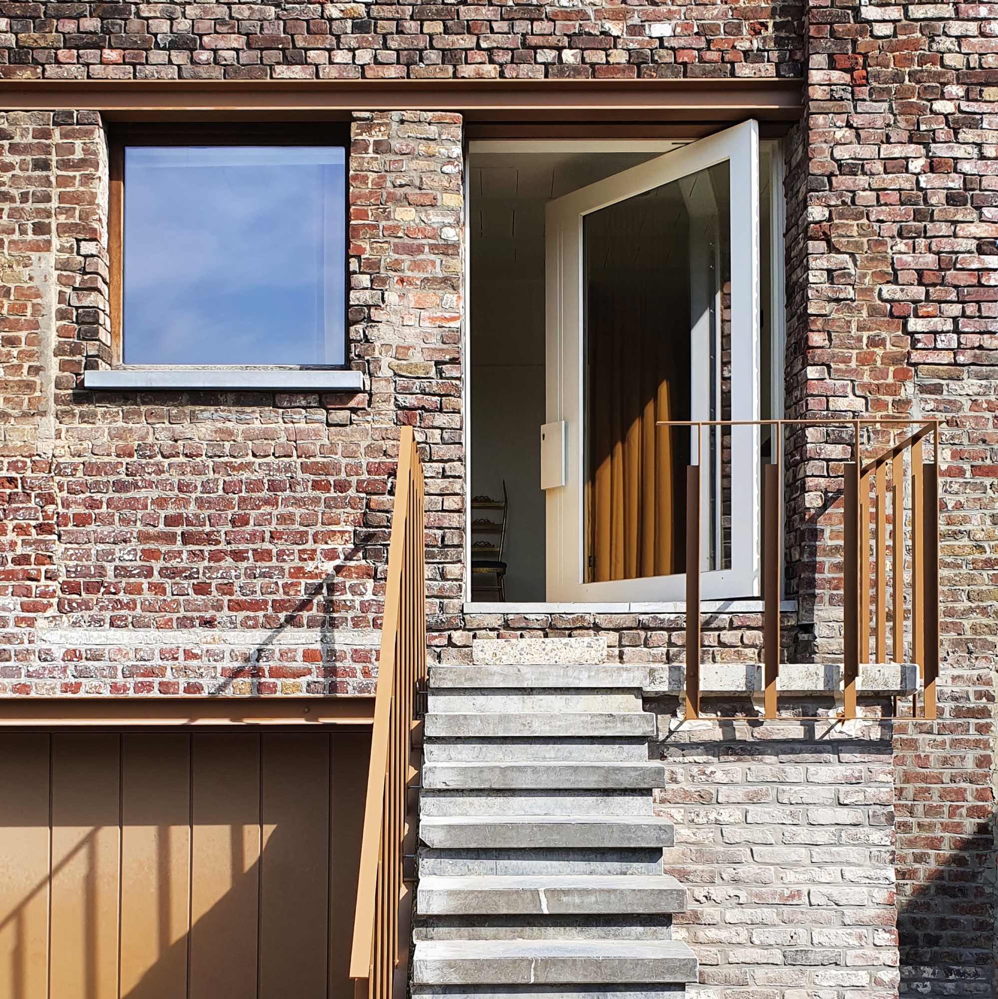 Outdoor stair with timber handrail ascending to glazed doorway framed by weathered brick