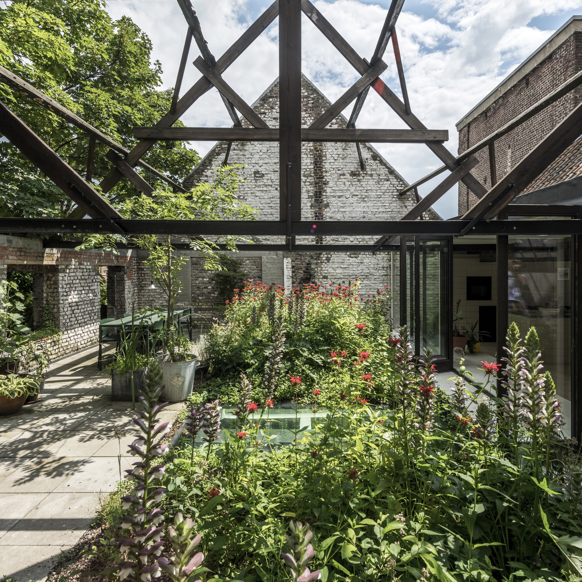 Planted courtyard garden under a steel-framed pergola structure with white brick walls beyond