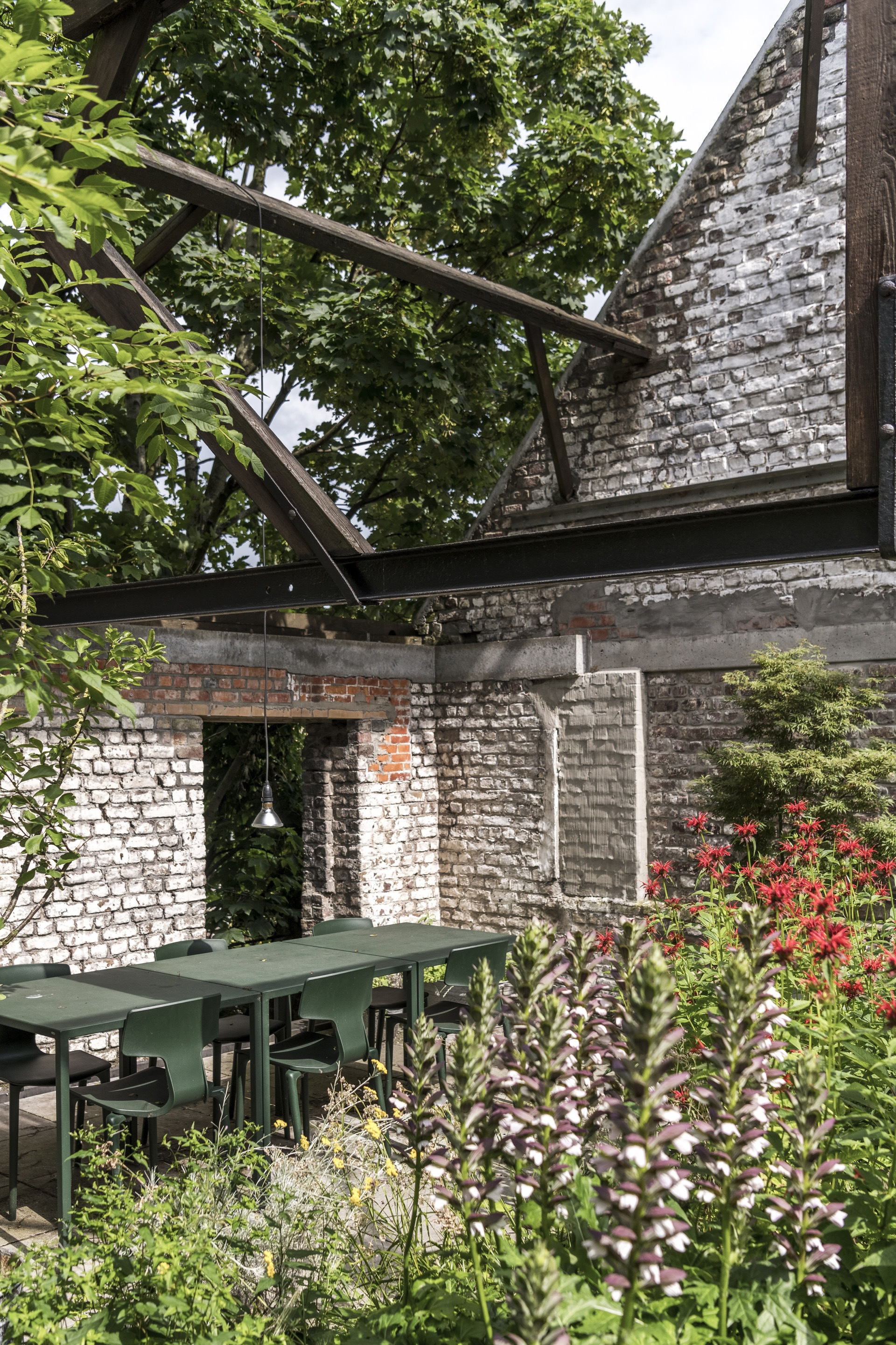 Garden dining area with steel table under painted brick walls and angled timber beams among flowering plants