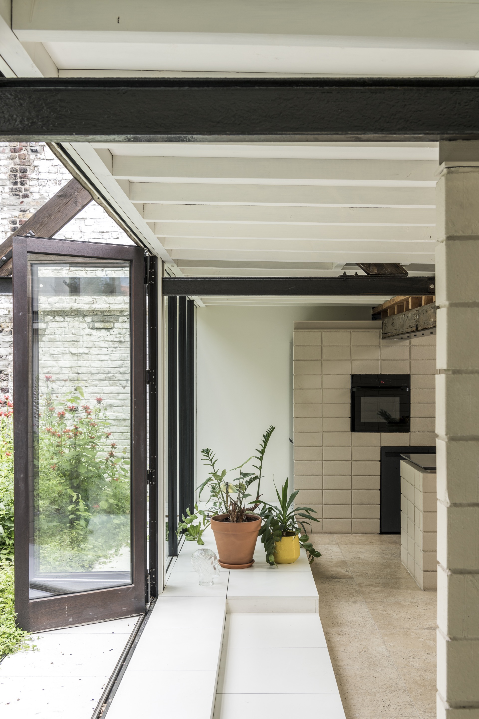 Open folding glass door leading to a planted courtyard with potted plants on the interior sill
