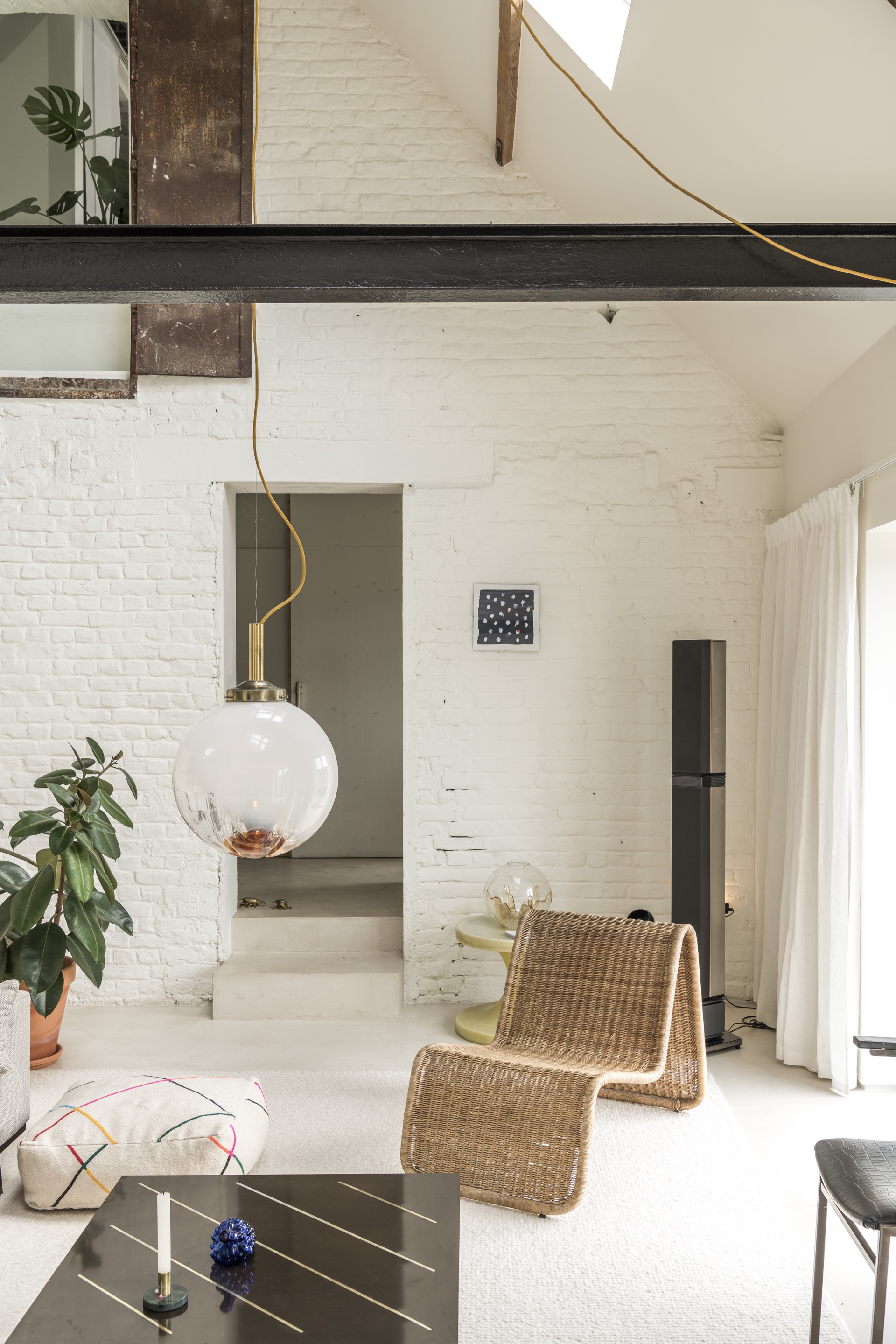 Double-height living space with exposed white brick walls, dark structural beam, and spherical pendant light
