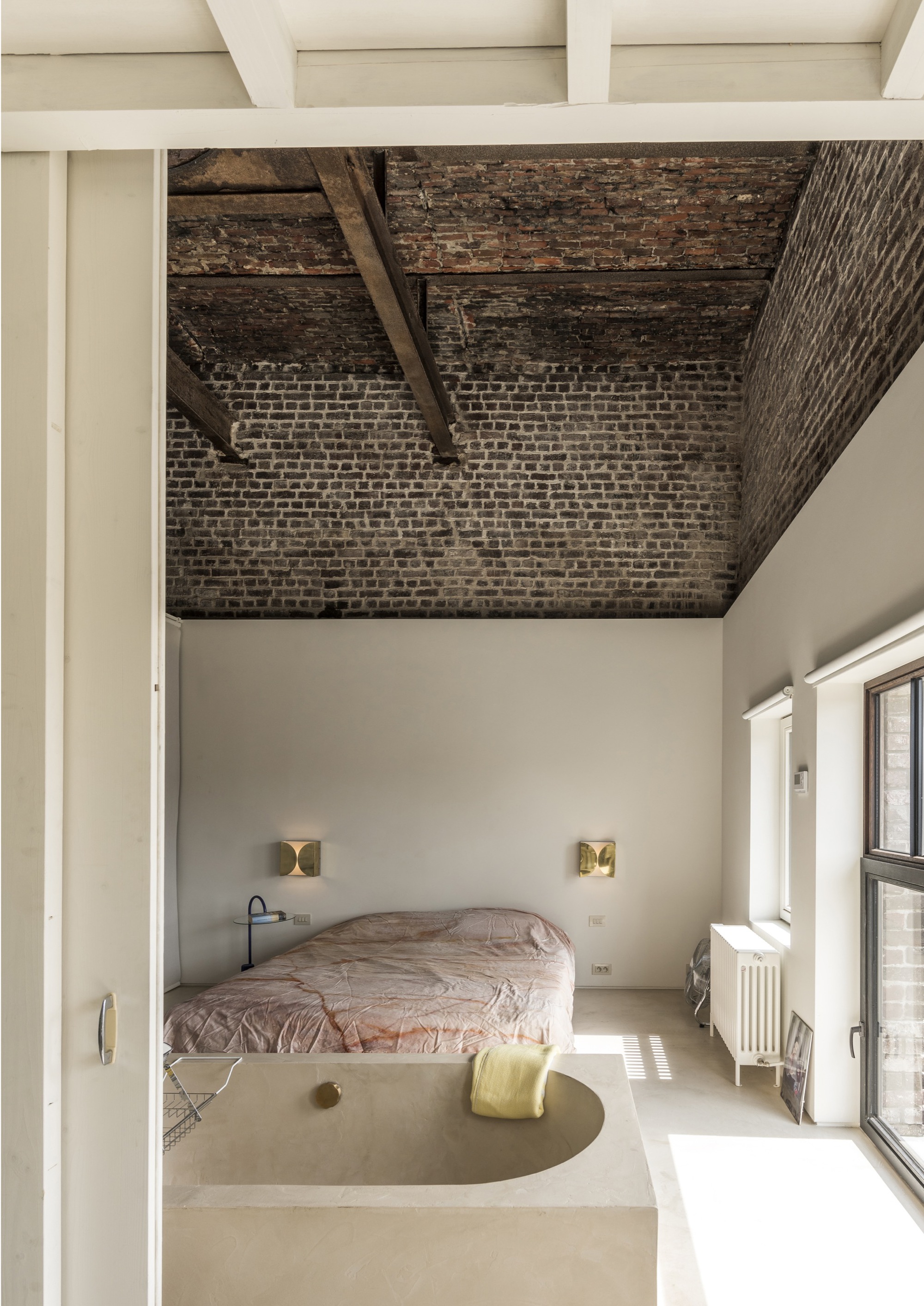 Bedroom with exposed brick ceiling vault, timber beams, and raised platform bed framed by white walls