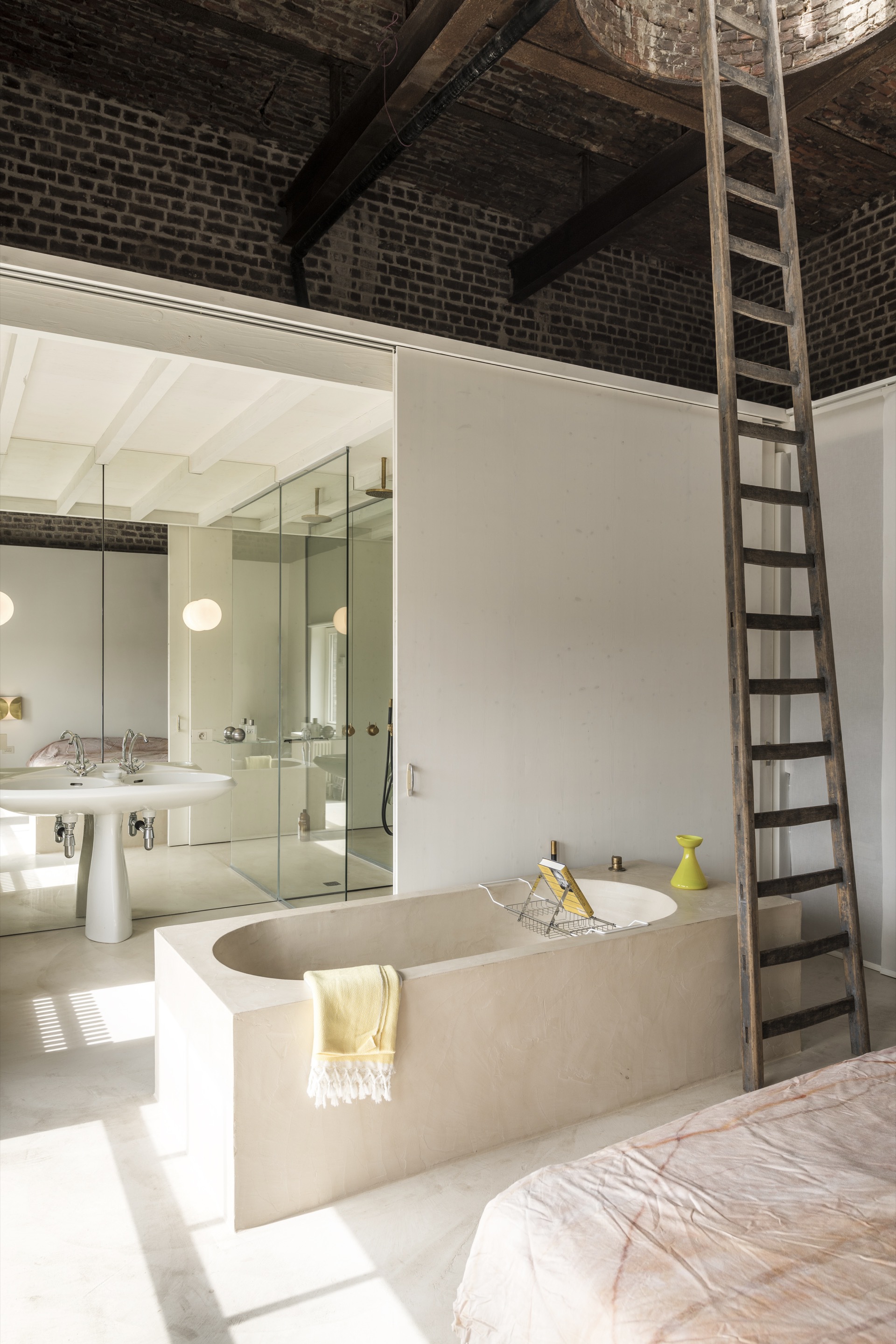 Bathroom with sunken concrete tub, glass shower enclosure, and narrow ladder ascending to exposed brick vault