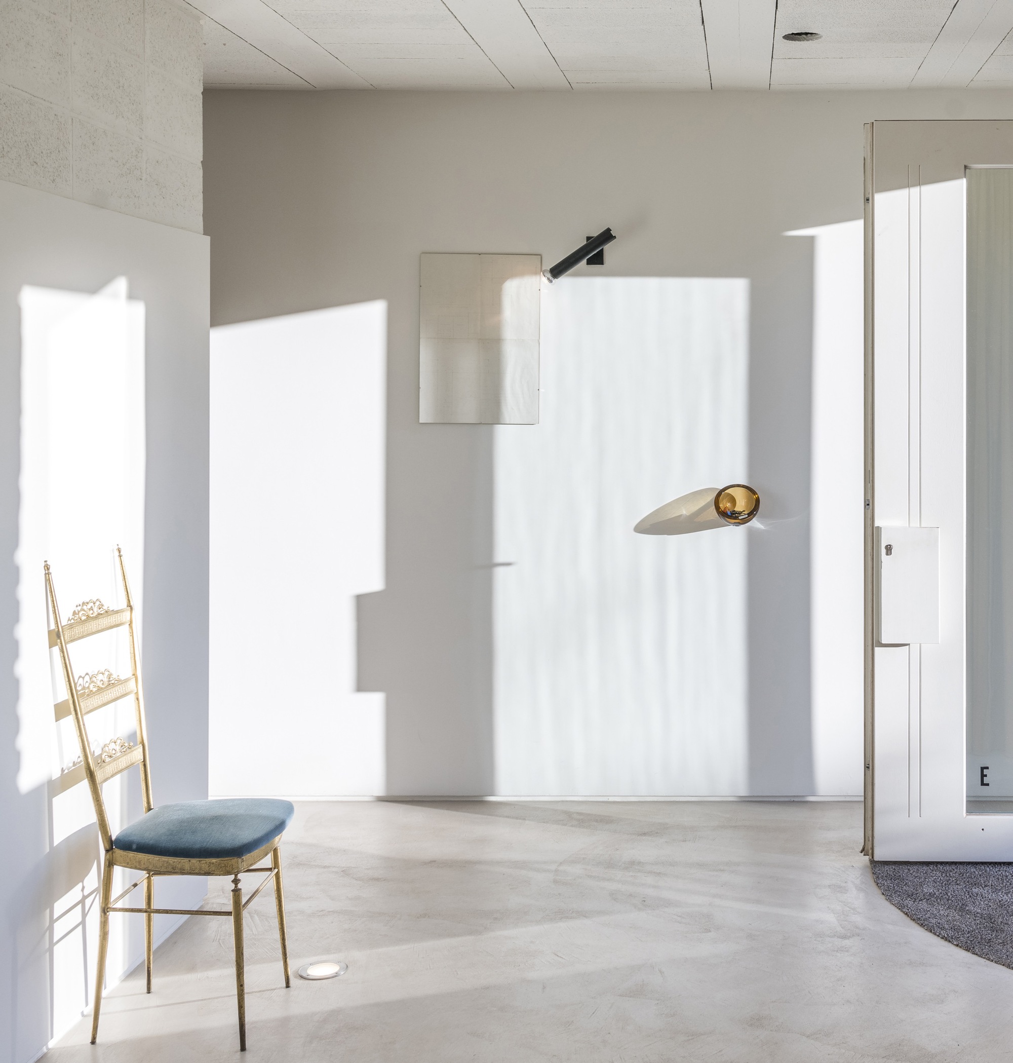 Interior room with concrete floor, timber ladder chair and sharp sunlight patterns across white walls