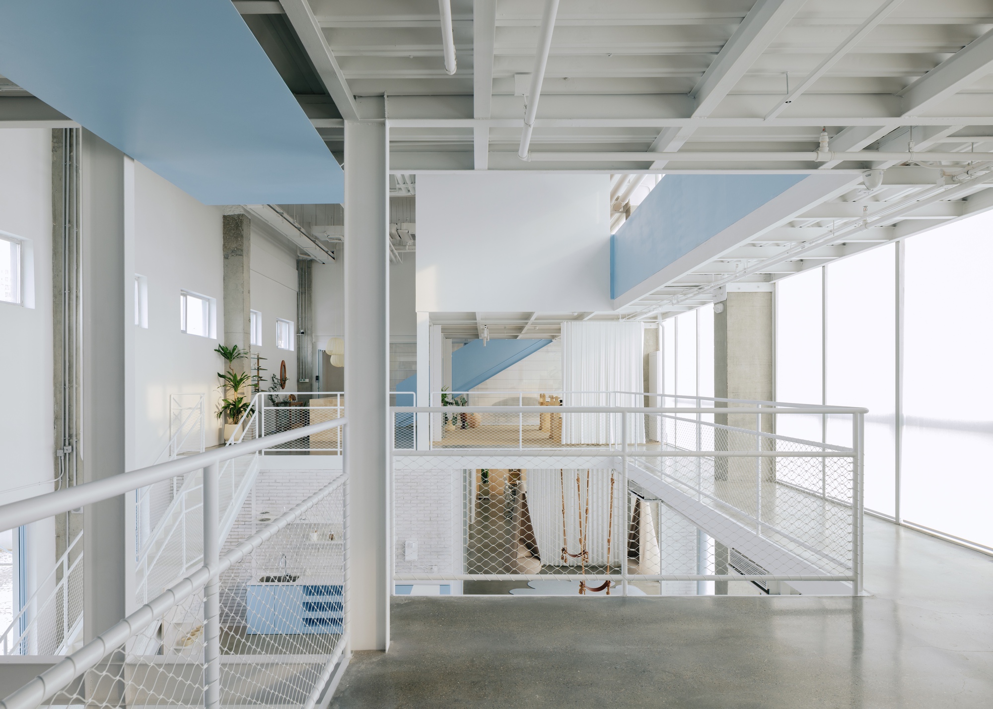 Double-height interior with white metal mesh railings and exposed timber joist ceiling over polished concrete floors