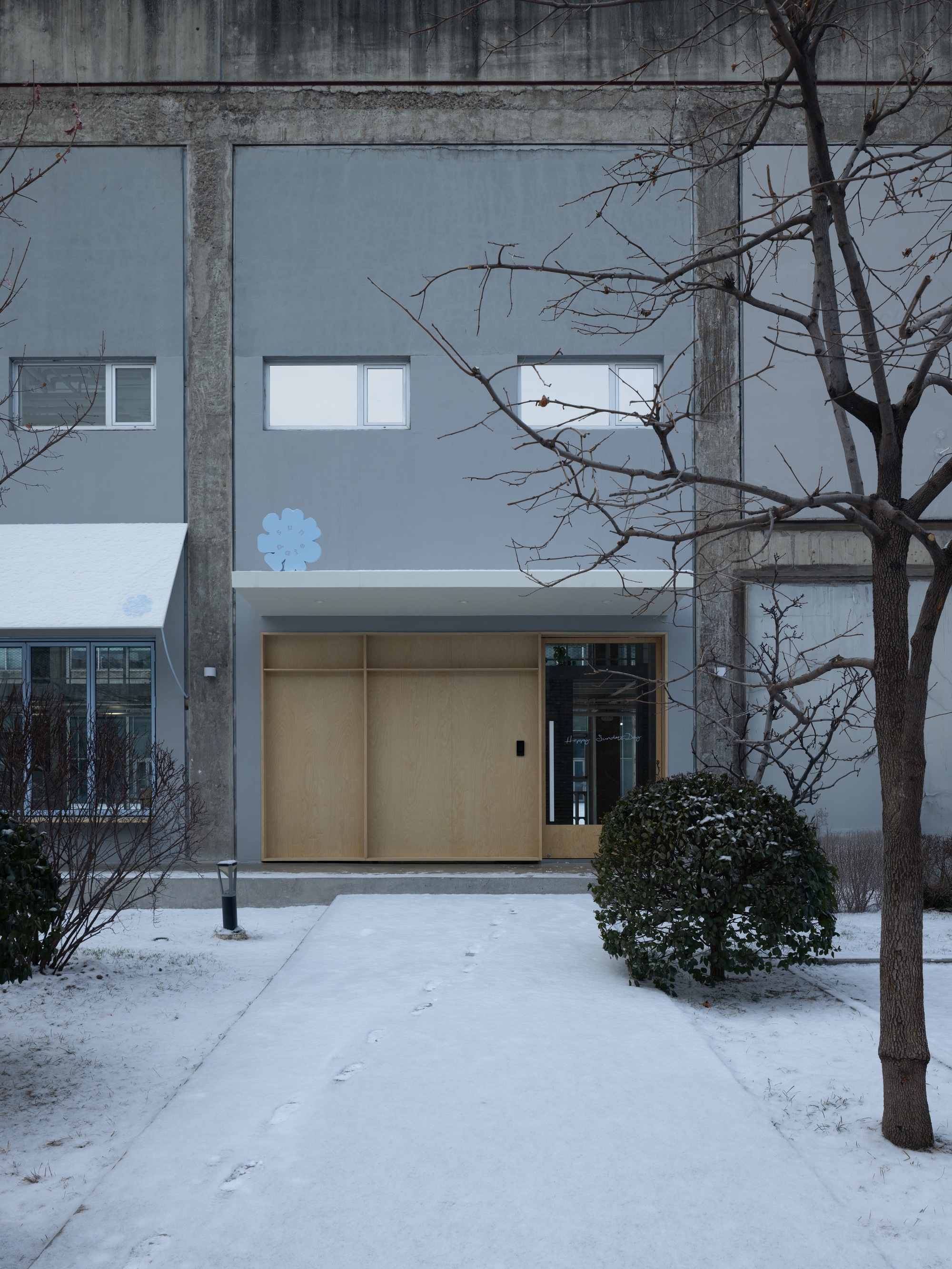 Entrance with light wood sliding doors framed by concrete columns and bare winter trees in snow