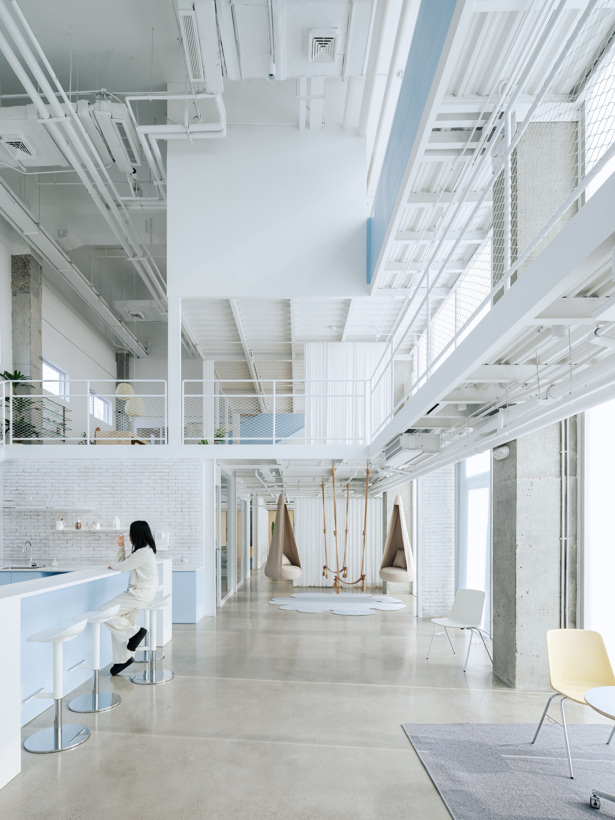 Ground floor lounge with white tile walls, rope swings and a person seated at a high counter