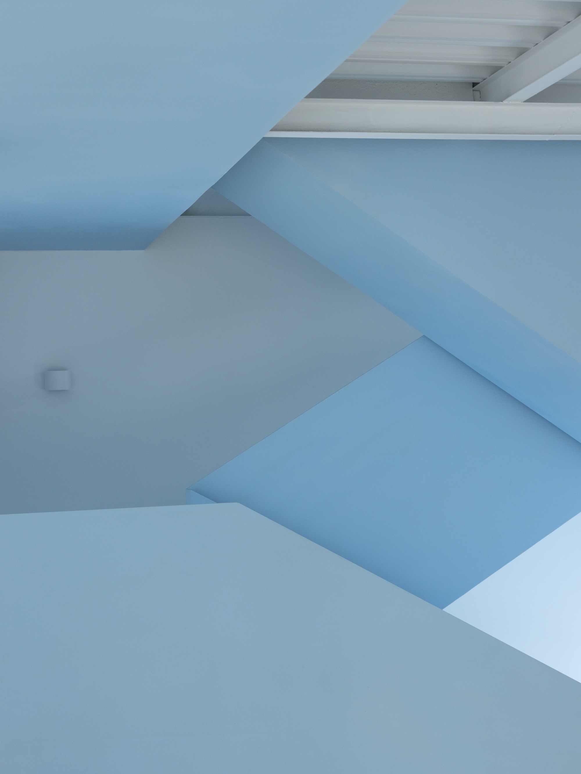 Close view of the folded blue stair soffit and white wall planes under daylight