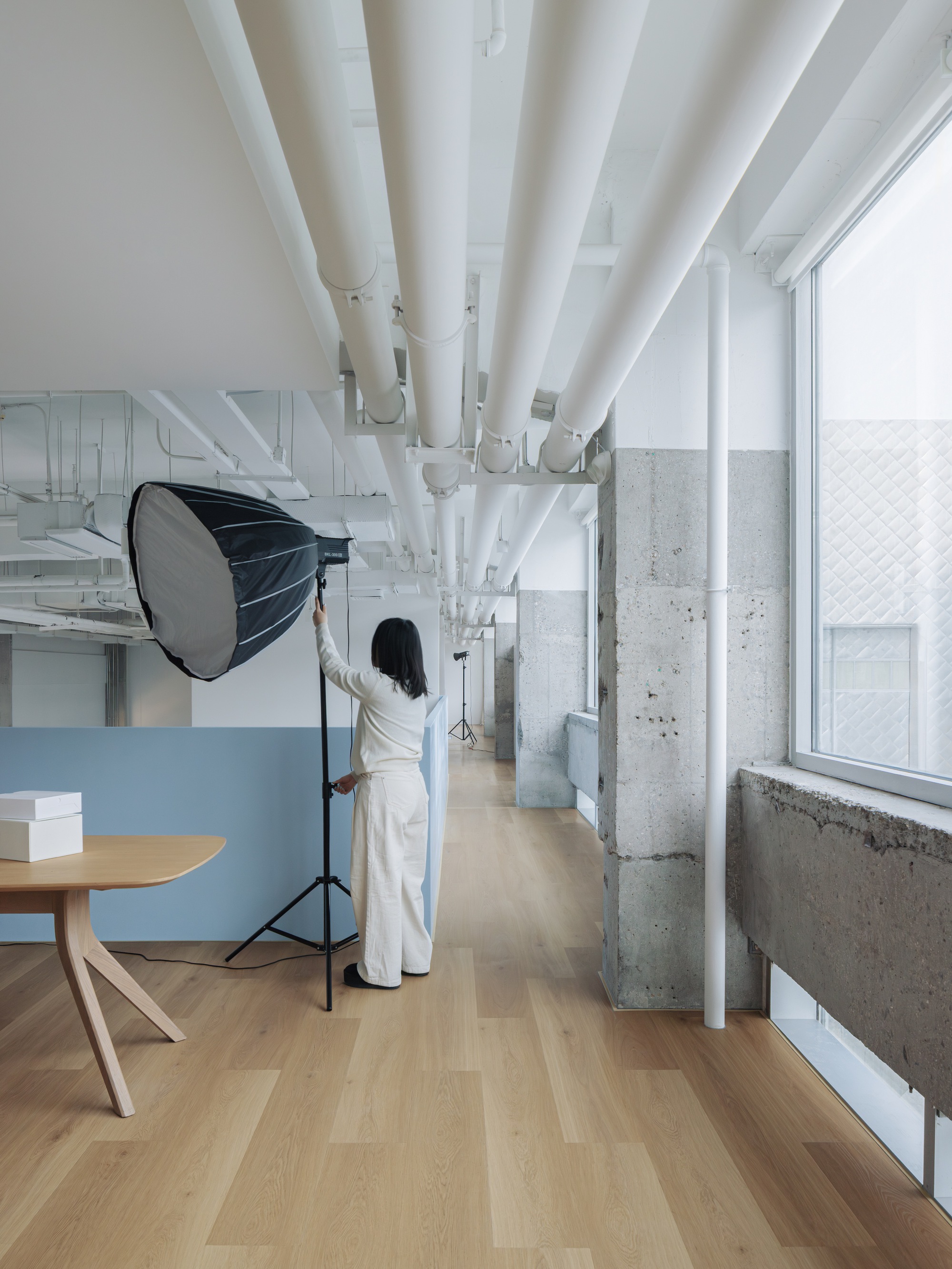Corridor with radiating white structural beams overhead and person adjusting studio lighting near concrete columns