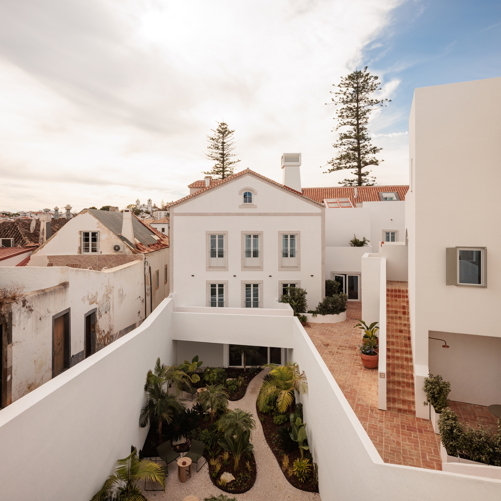 Courtyard with planted beds and terracotta paving overlooking a traditional tile-roofed building beyond