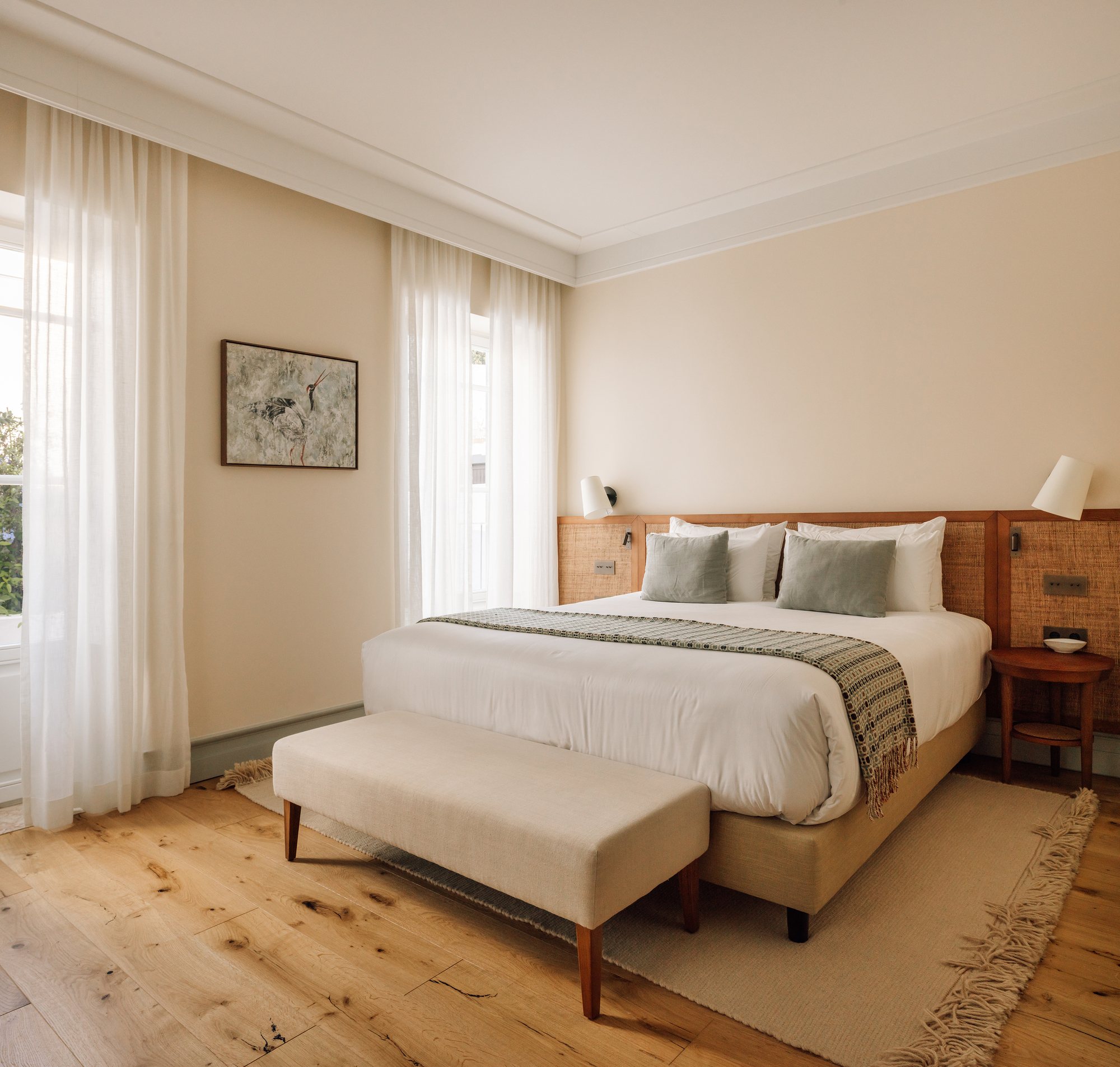 Bedroom with timber headboard, knotted pine flooring and sheer curtains filtering daylight