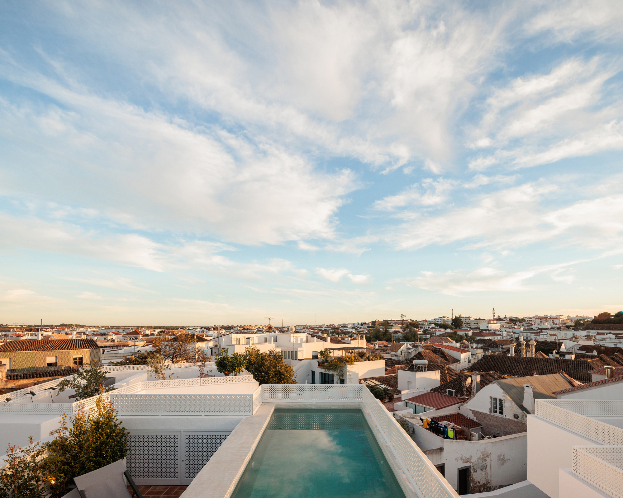 Rooftop pool with perforated white screening overlooking terracotta rooftops at dusk