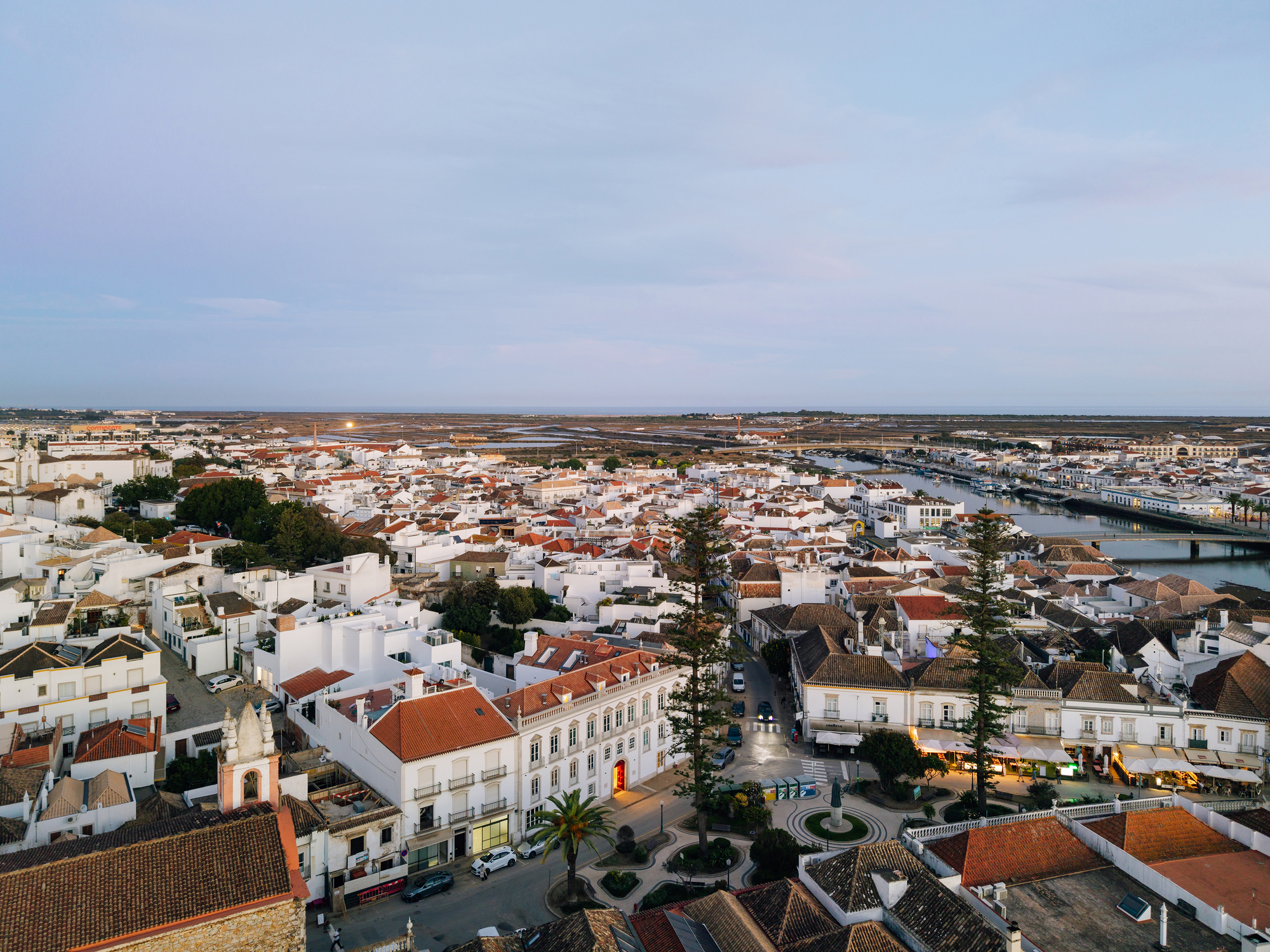 Aerial view of whitewashed rooftops and terracotta tiles spreading toward distant wetlands under evening light
