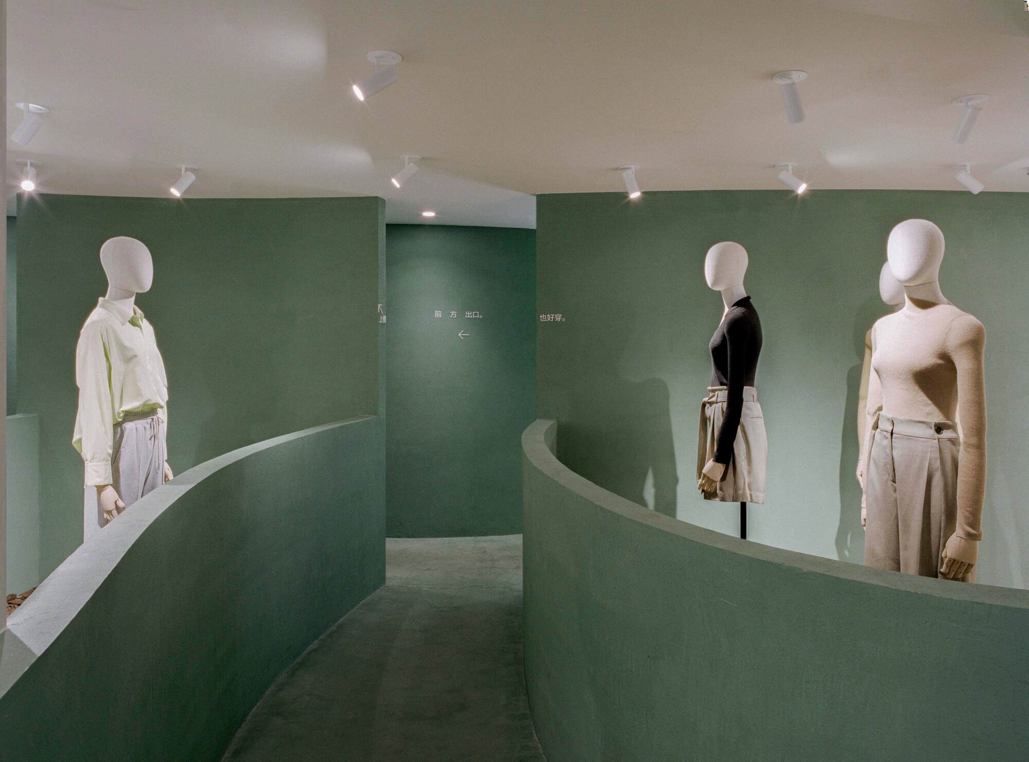 Interior retail space with curving green partition walls and white mannequins displaying clothing