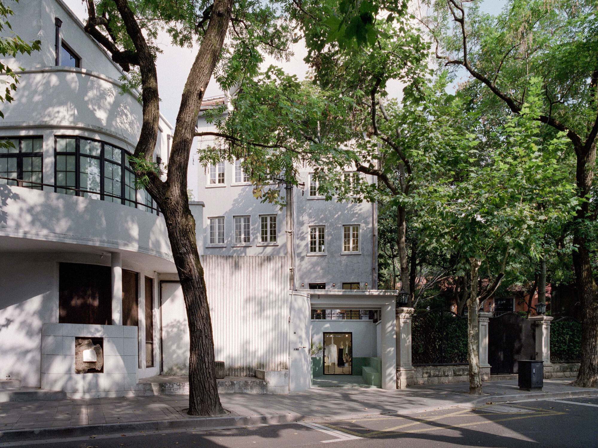 Street view of white facade insertion between historic buildings framed by mature deciduous trees