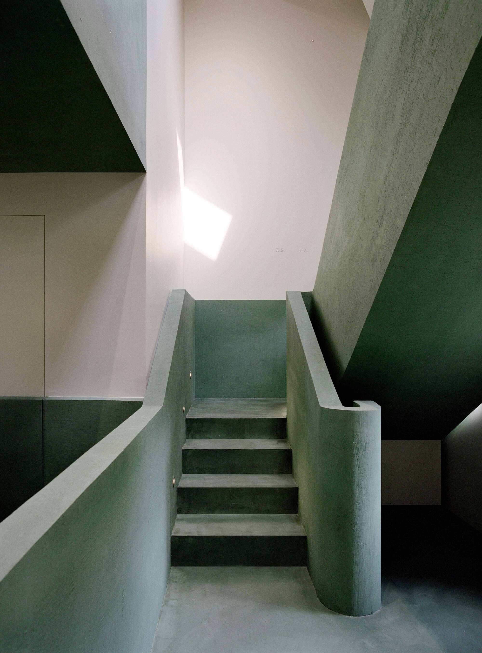Stairwell with green plaster walls and cylindrical column rising to a skylight above
