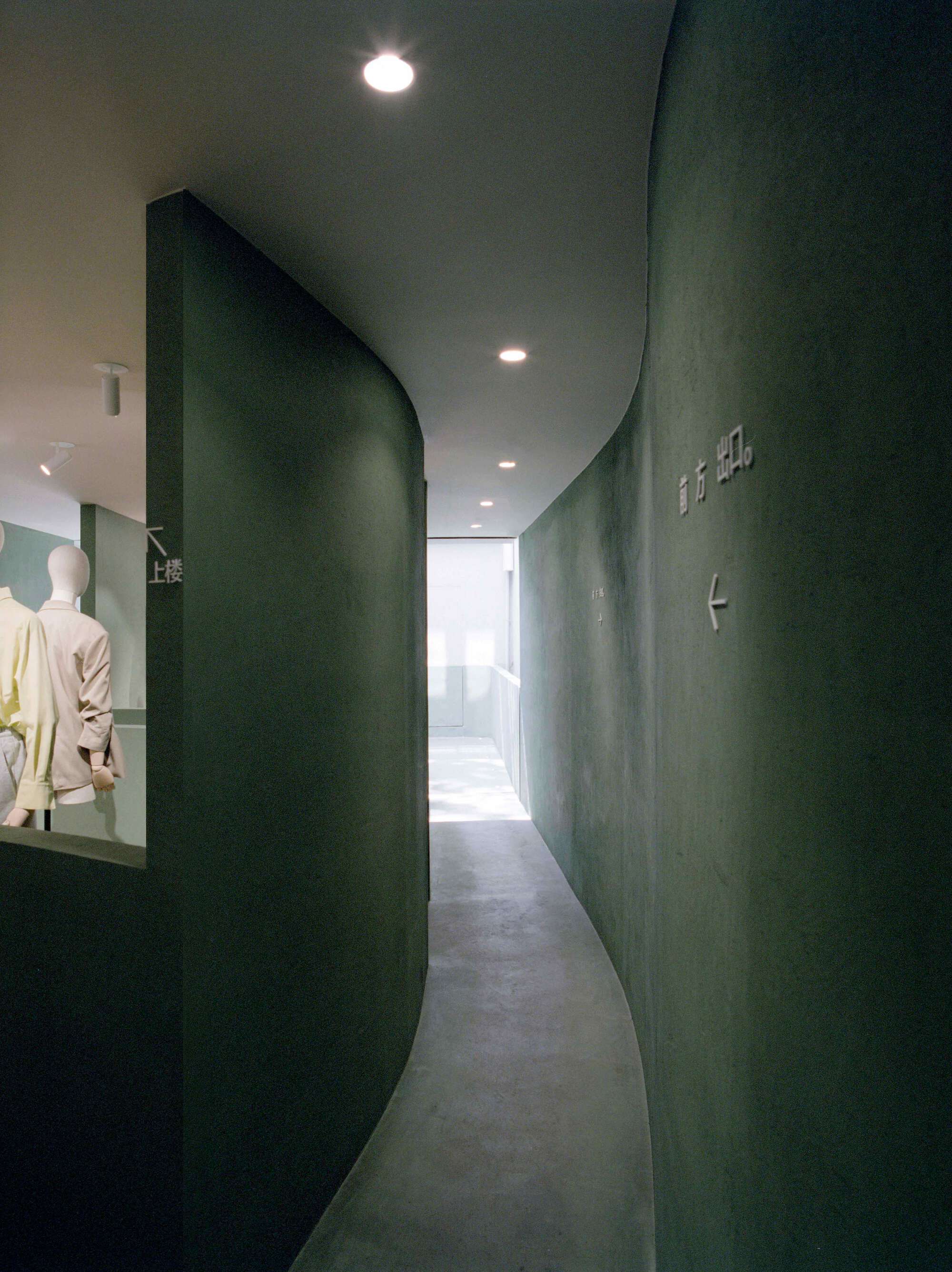 Curved green plaster wall forming a passage with recessed lighting overhead