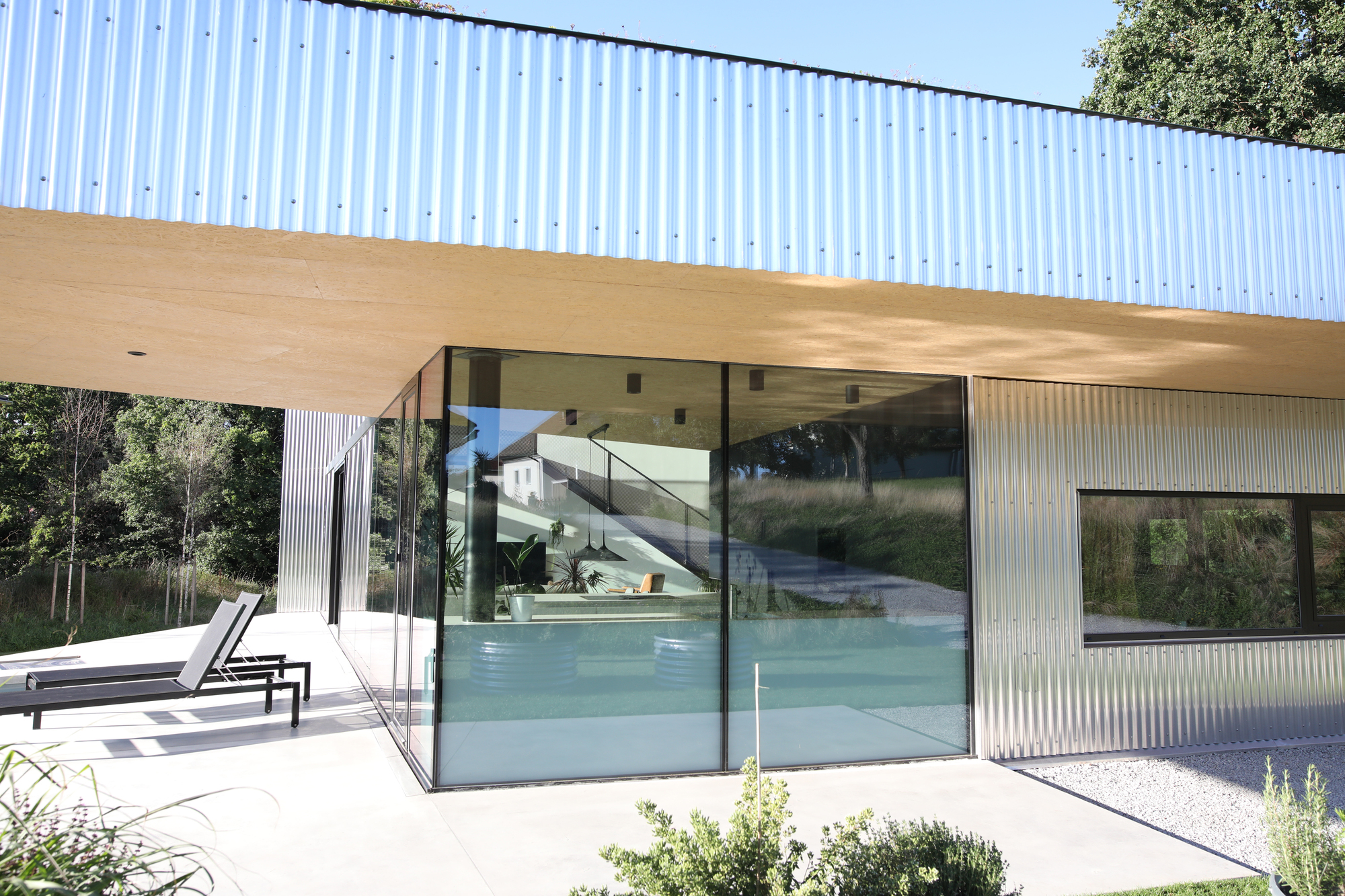 Poolside terrace with floor-to-ceiling glass sliding doors below the corrugated metal soffit overhang