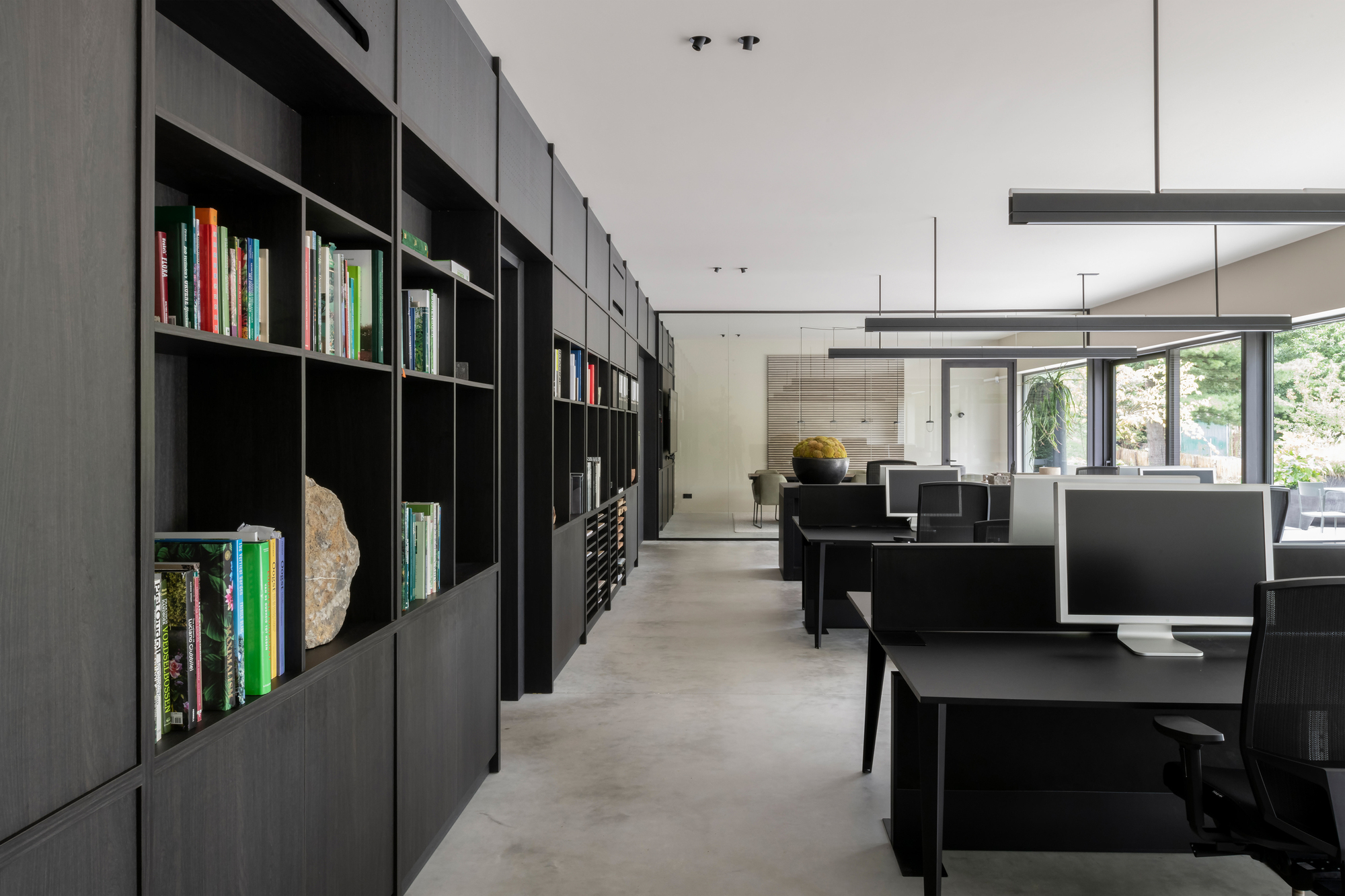 Open office interior with black modular shelving along one wall and workstations beneath linear pendant lights