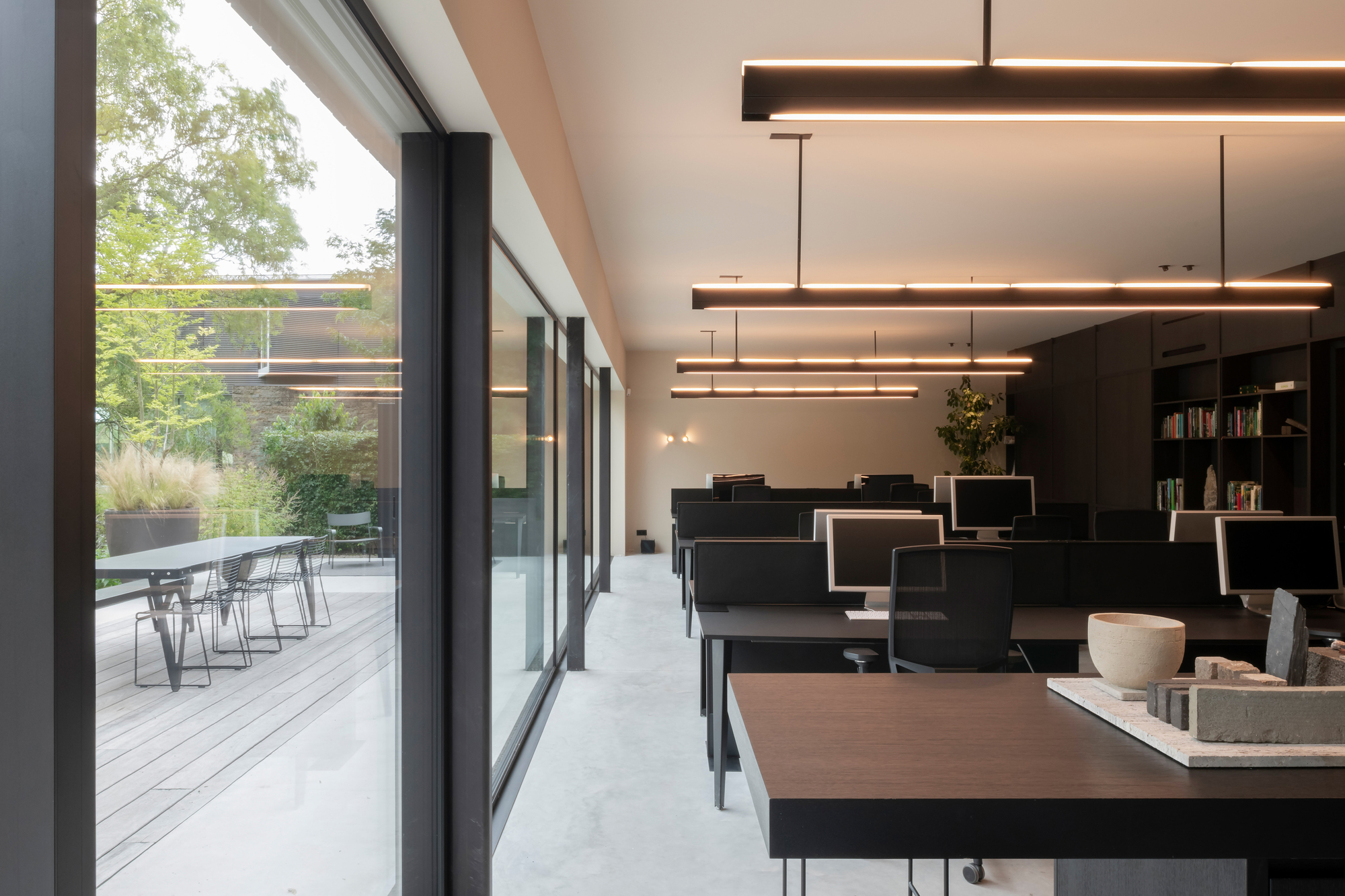 Office interior with black workstations and suspended linear lighting opening to a timber deck terrace