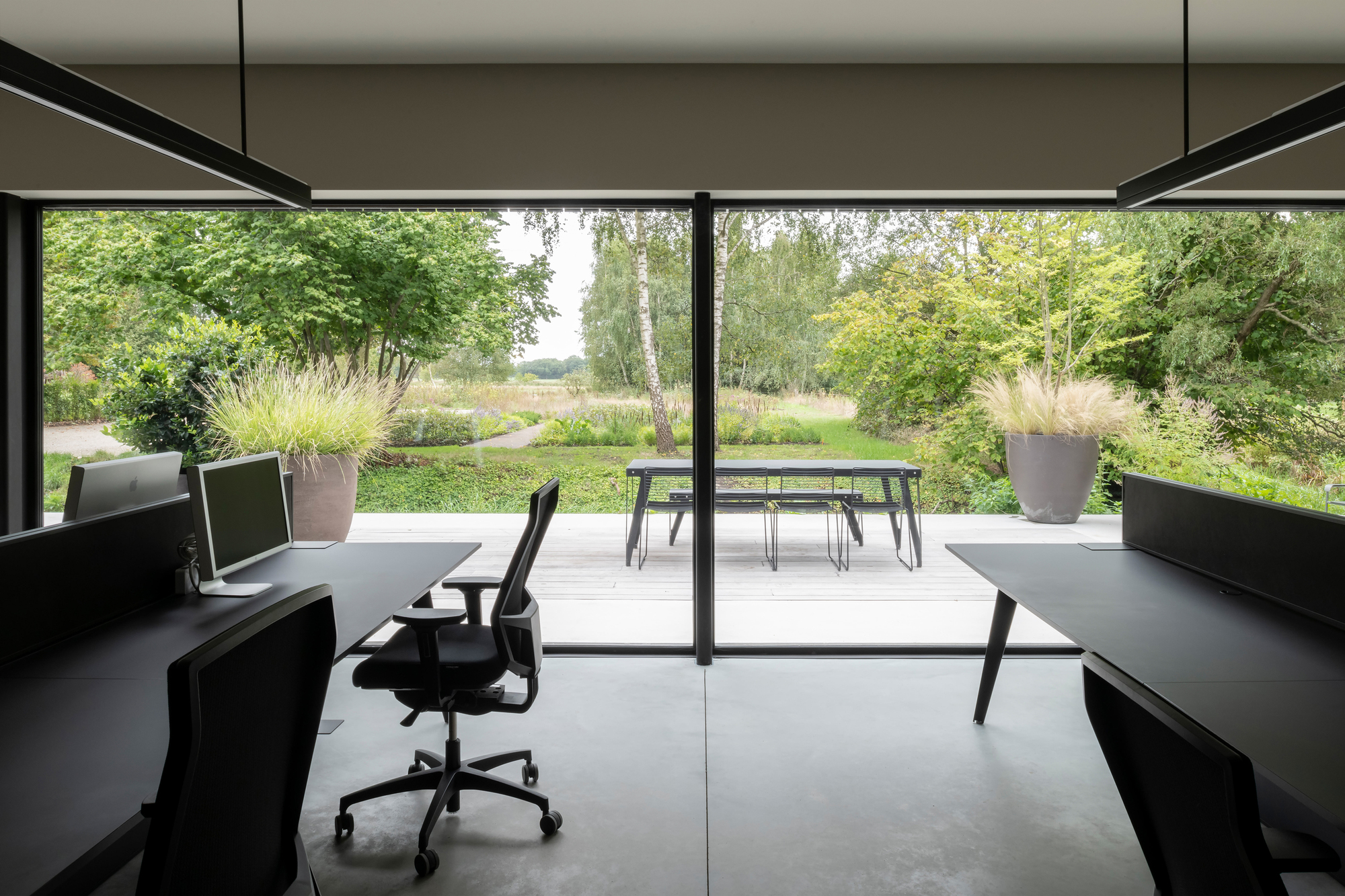 Workspace with floor-to-ceiling glazing framing views of the grassy landscape and outdoor dining area