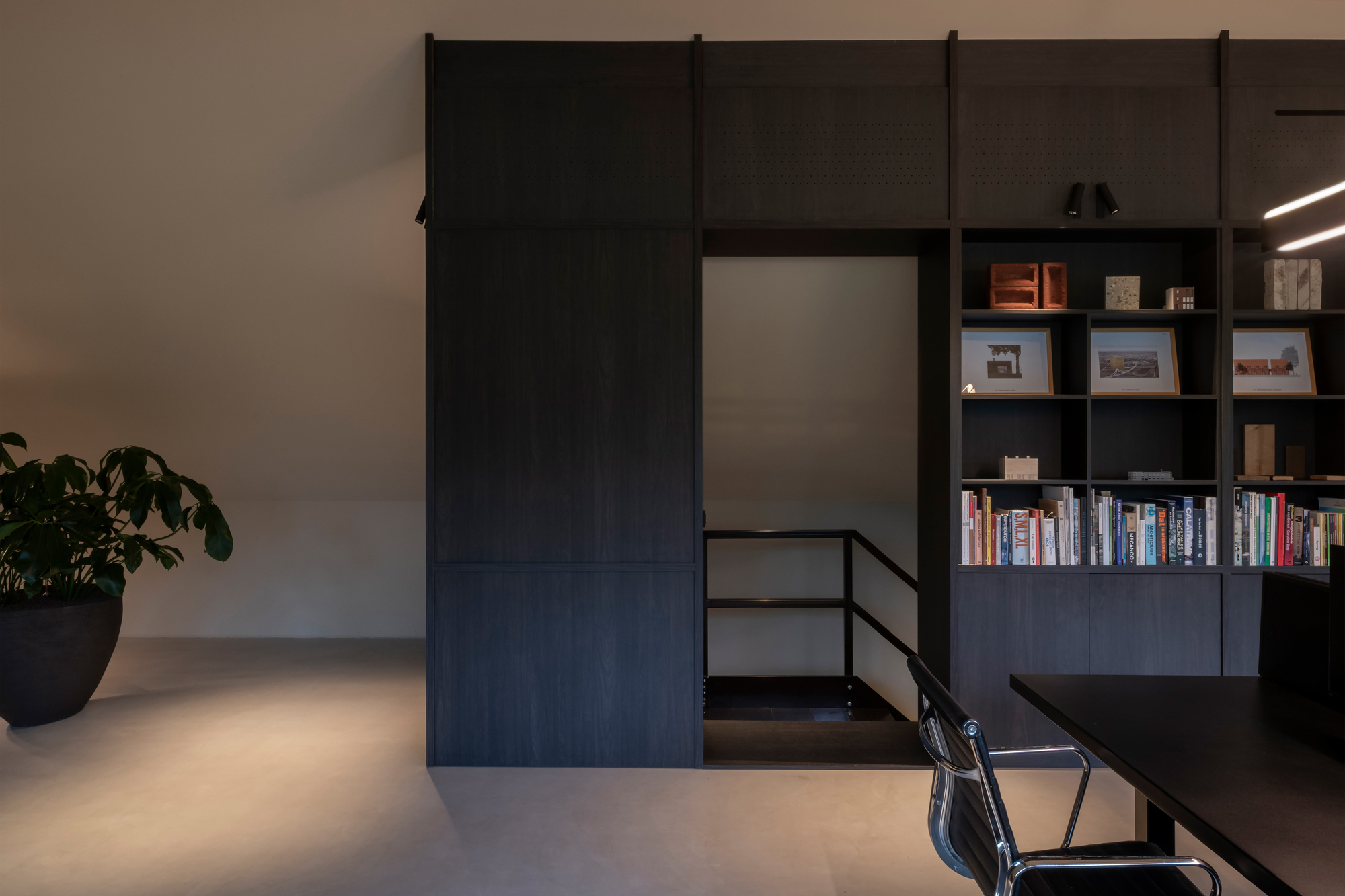 Black sliding barn door on steel track beside built-in shelving and polished concrete floor