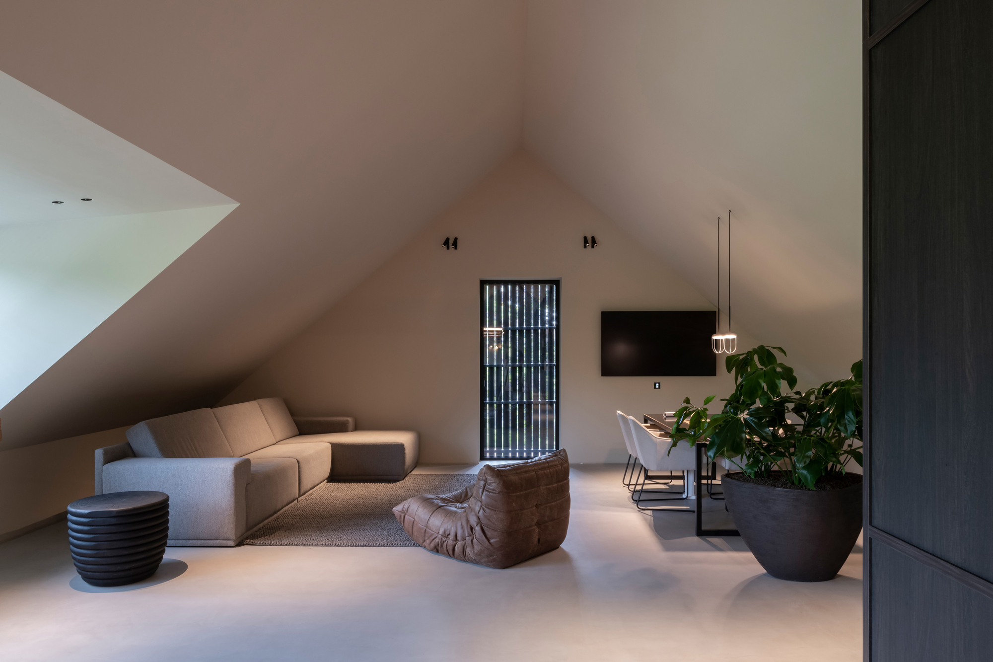 Upper level lounge beneath the sloped plaster ceiling with fluted glass door and potted greenery
