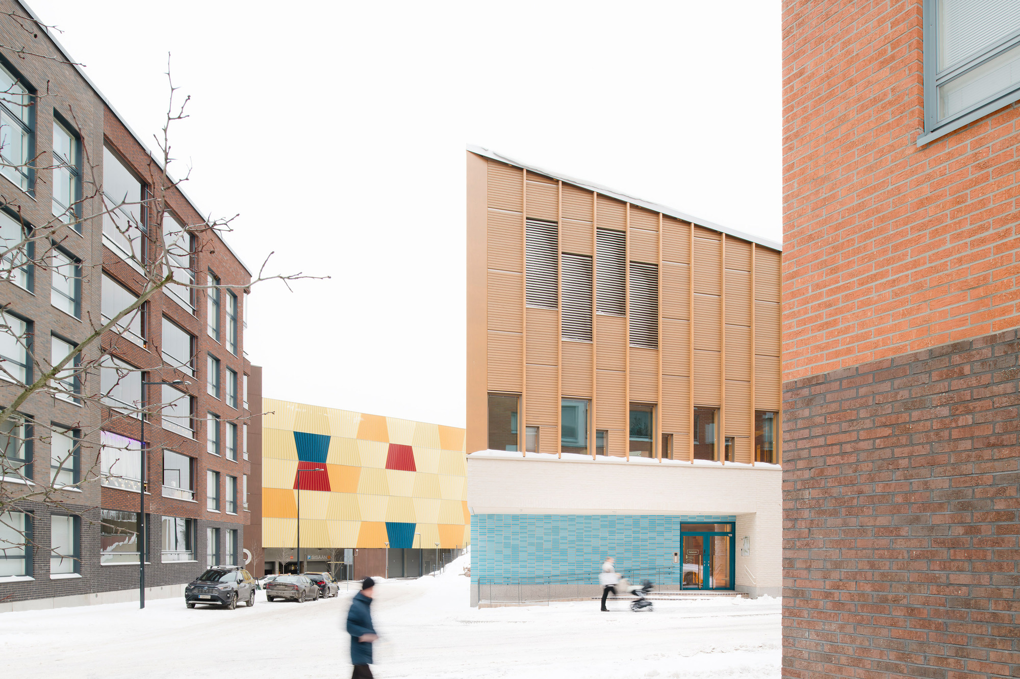 Street view showing the timber facade and colorful tiled wall between residential buildings with pedestrians in winter