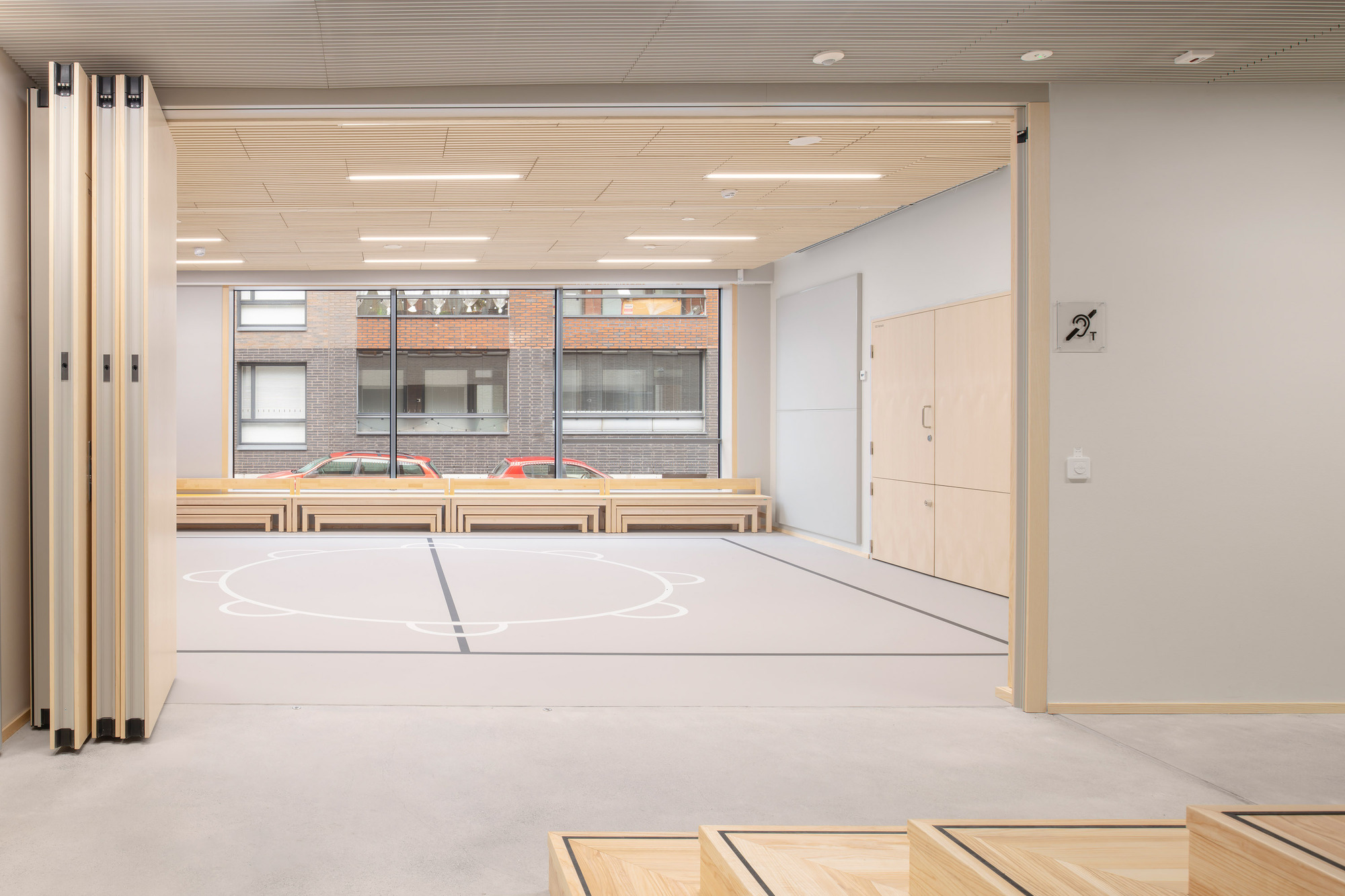 Multipurpose interior space with folding partitions, timber benches, and acoustic ceiling panels under fluorescent lights