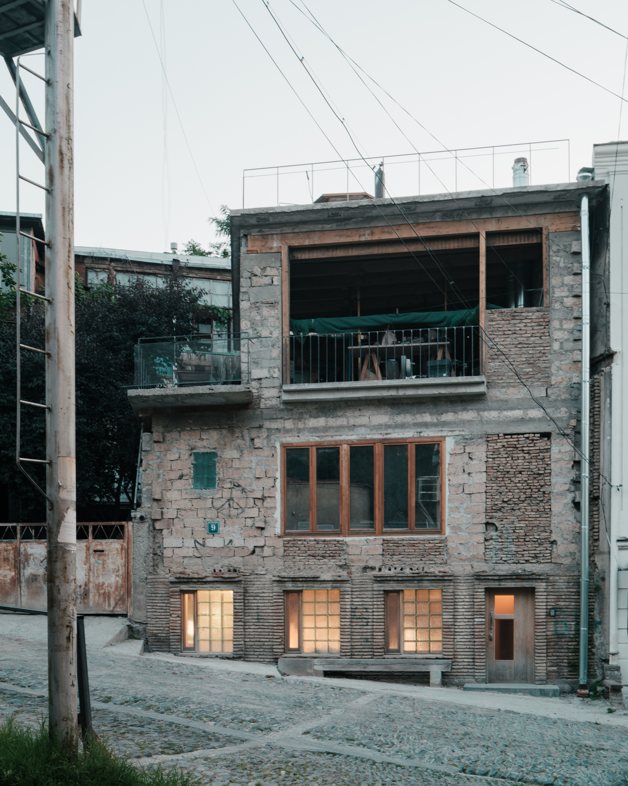 Three-story facade mixing concrete block, exposed brick, and timber fenestration at dusk