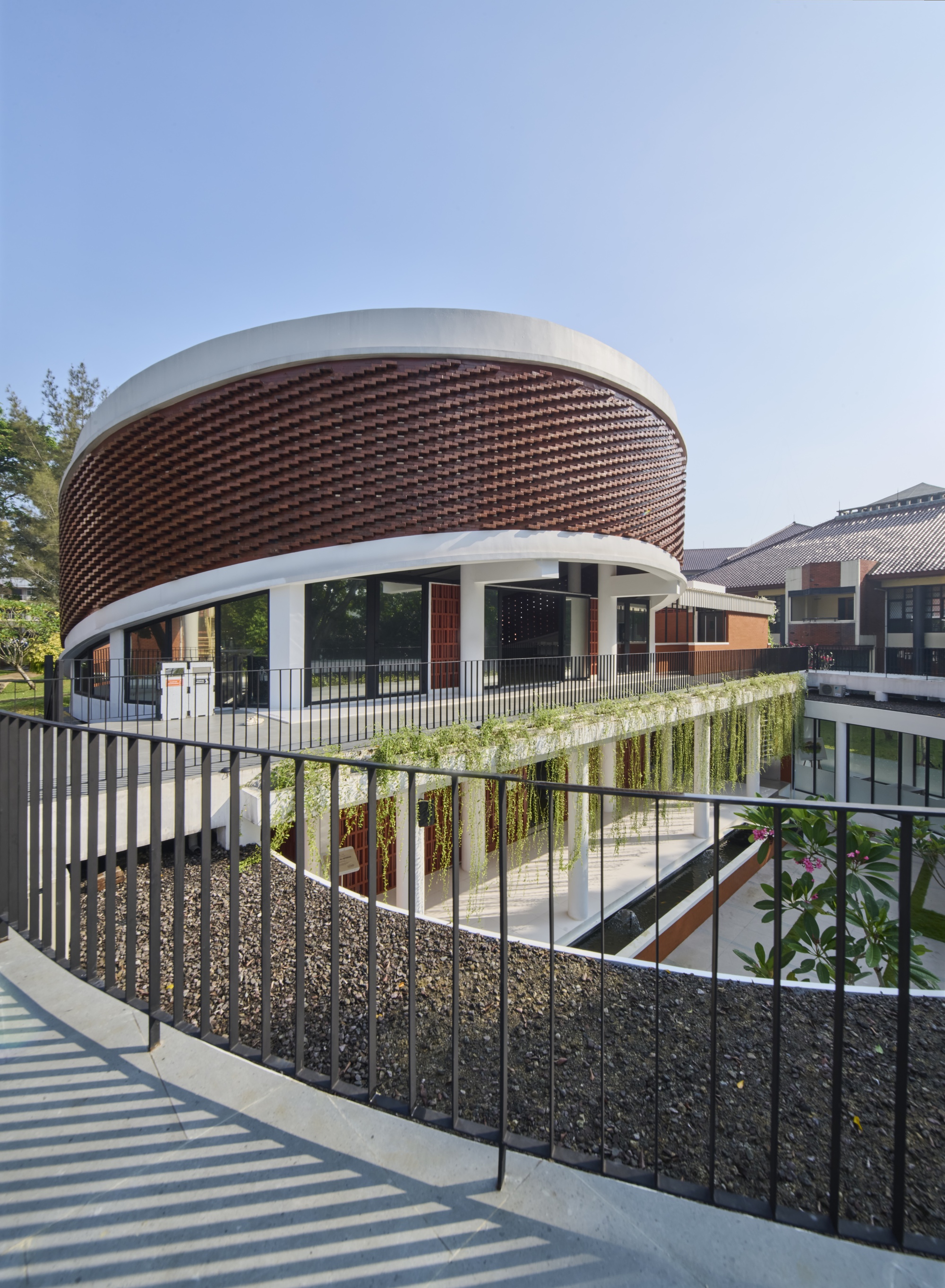 Curved staircase with metal railing leading to planted terrace below cylindrical basketweave brick facade