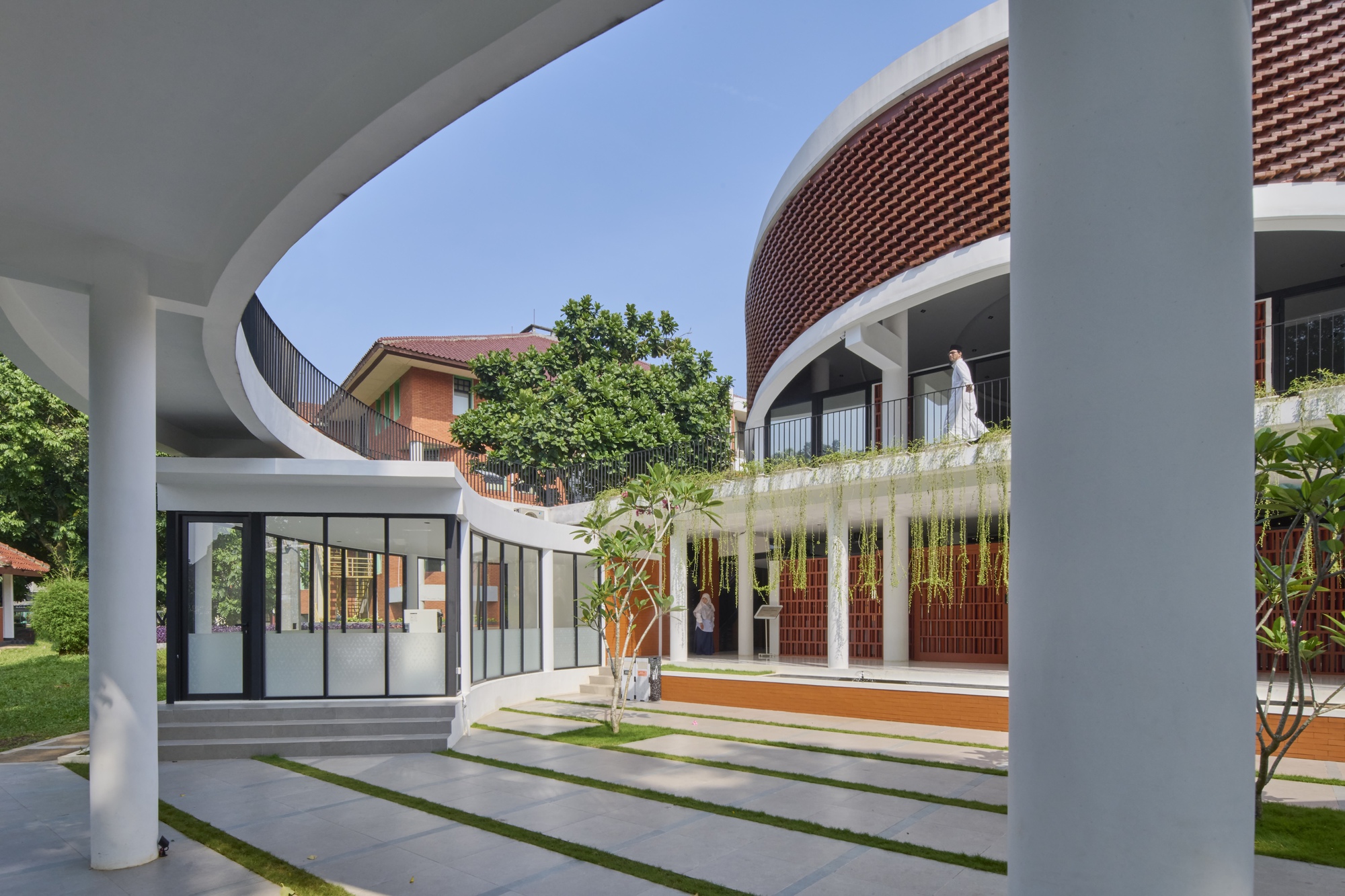 View through white columns framing courtyard with grass strips and person on upper terrace