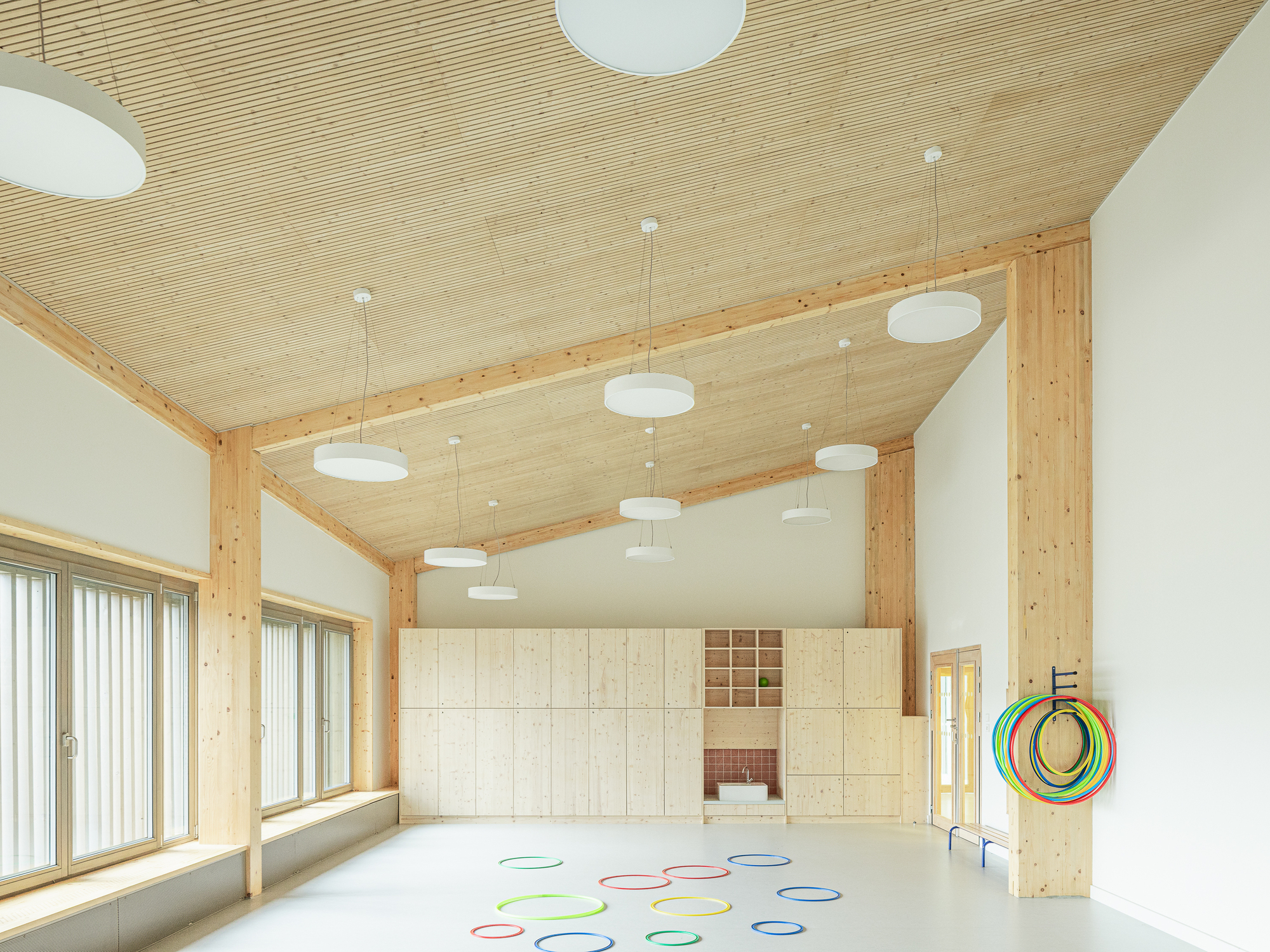 Interior room with ribbed timber ceiling, exposed beams, white pendant lights and colorful hoops on the floor
