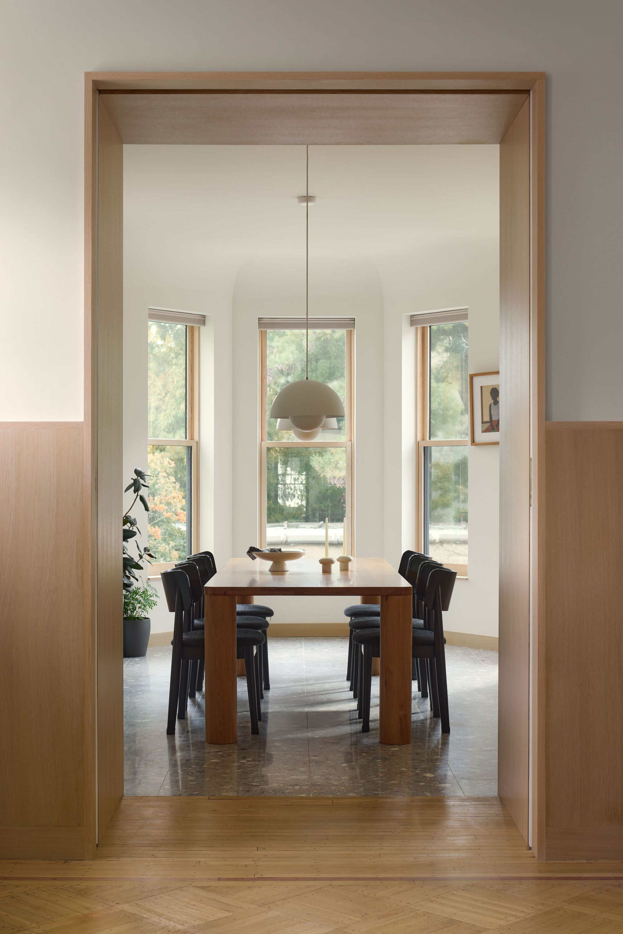 View through timber doorway to dining table and tall windows with tree foliage outside