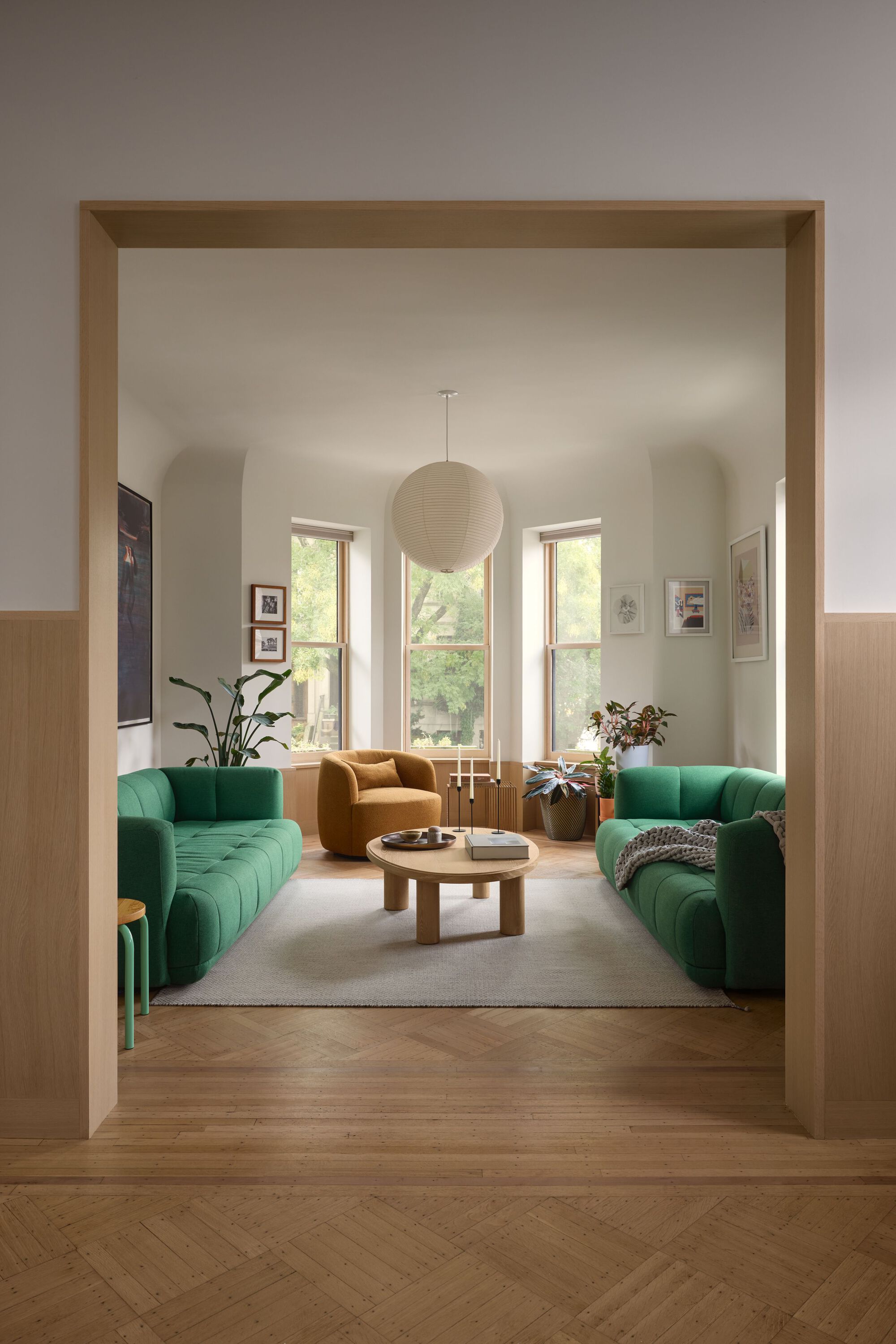 View through a timber-framed doorway into a living room with green upholstered sofas and tall windows
