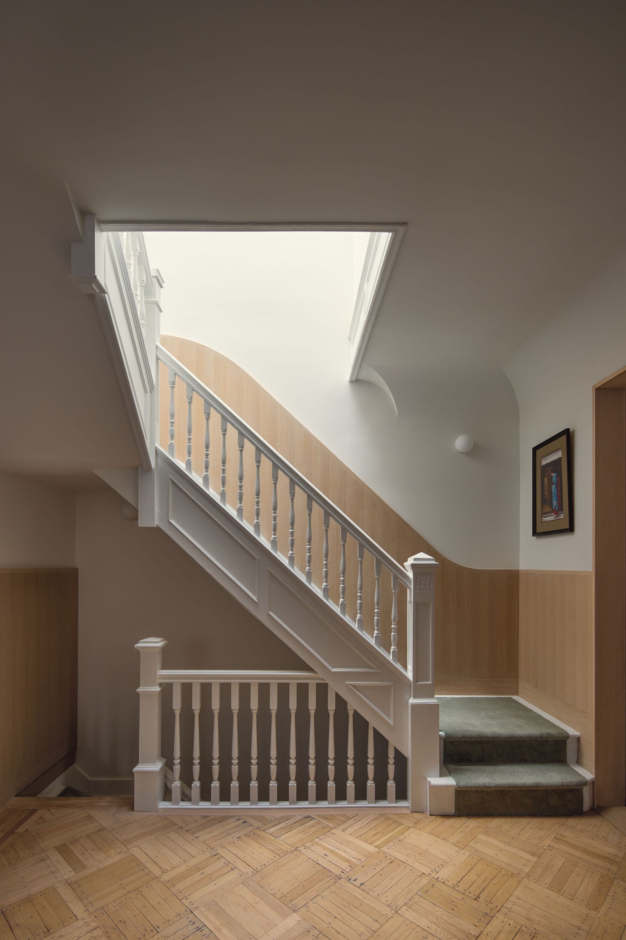Staircase with painted balustrade and timber handrail beneath a skylight with natural daylight
