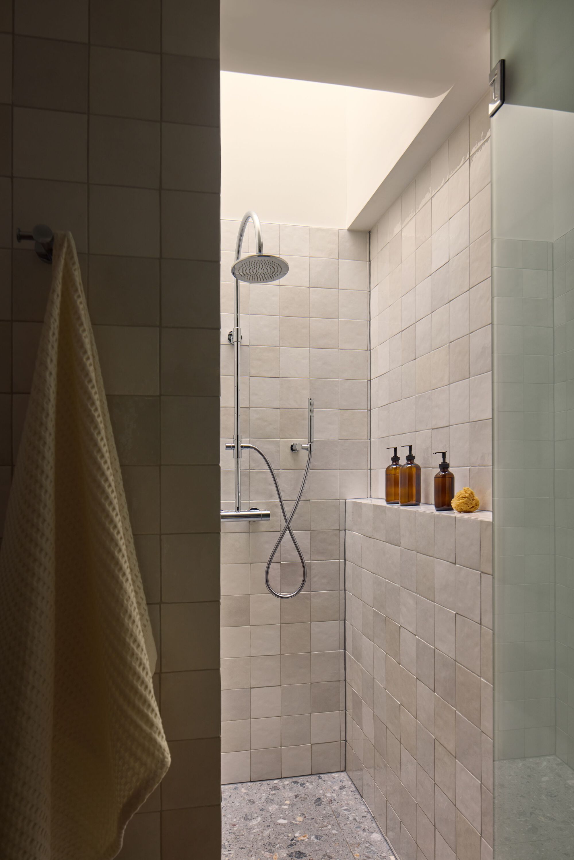 Shower enclosure with white tile walls and skylight casting angular sunlight onto the fixtures