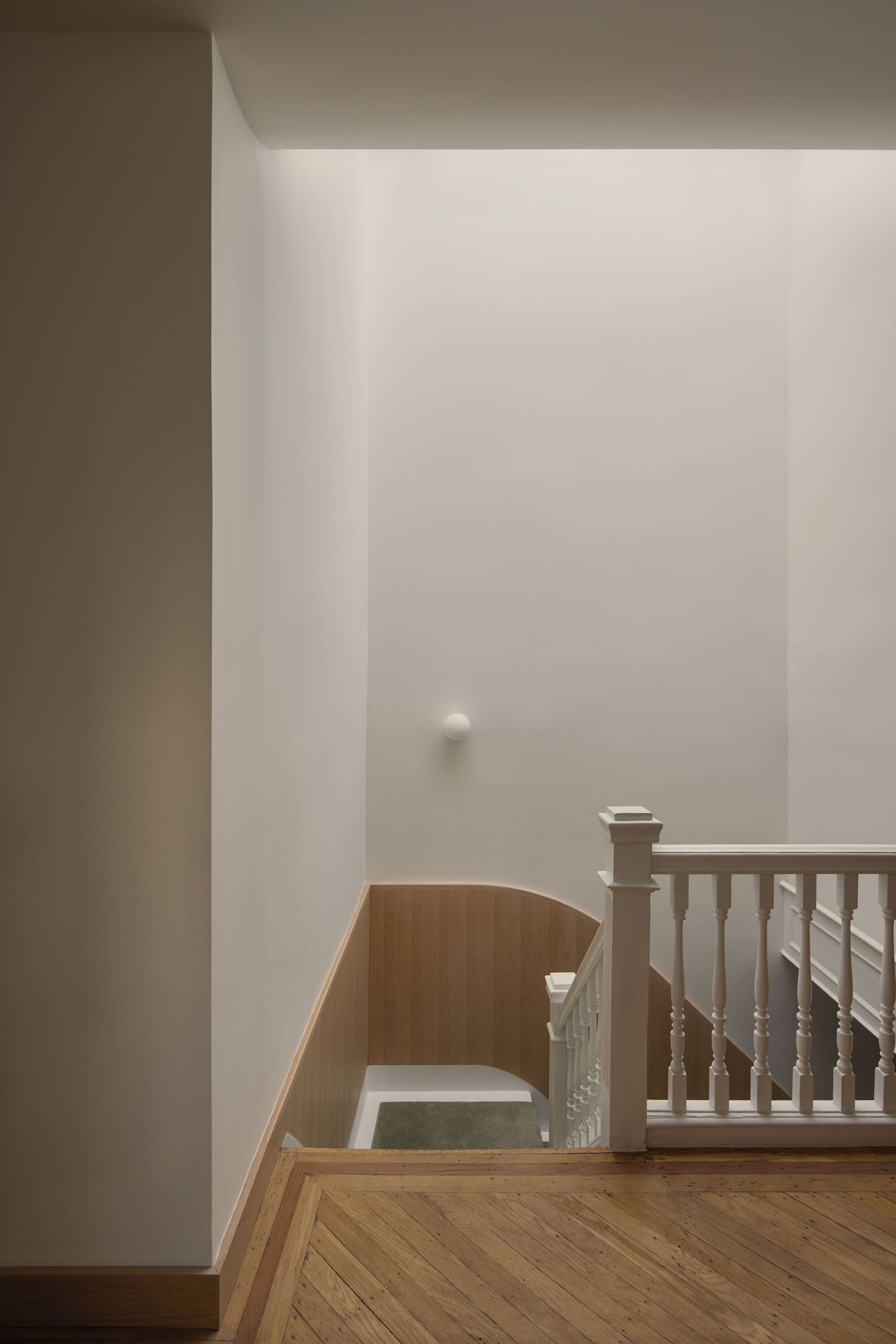 Landing with curved oak wall panels and herringbone timber flooring under soft ceiling light